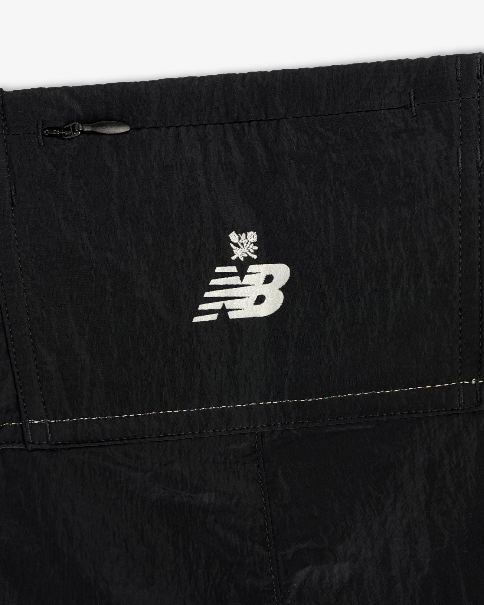 Close-up of black ALD / New Balance Lightweight Nylon Warmup Pant with a white logo and snowflake symbol above it.