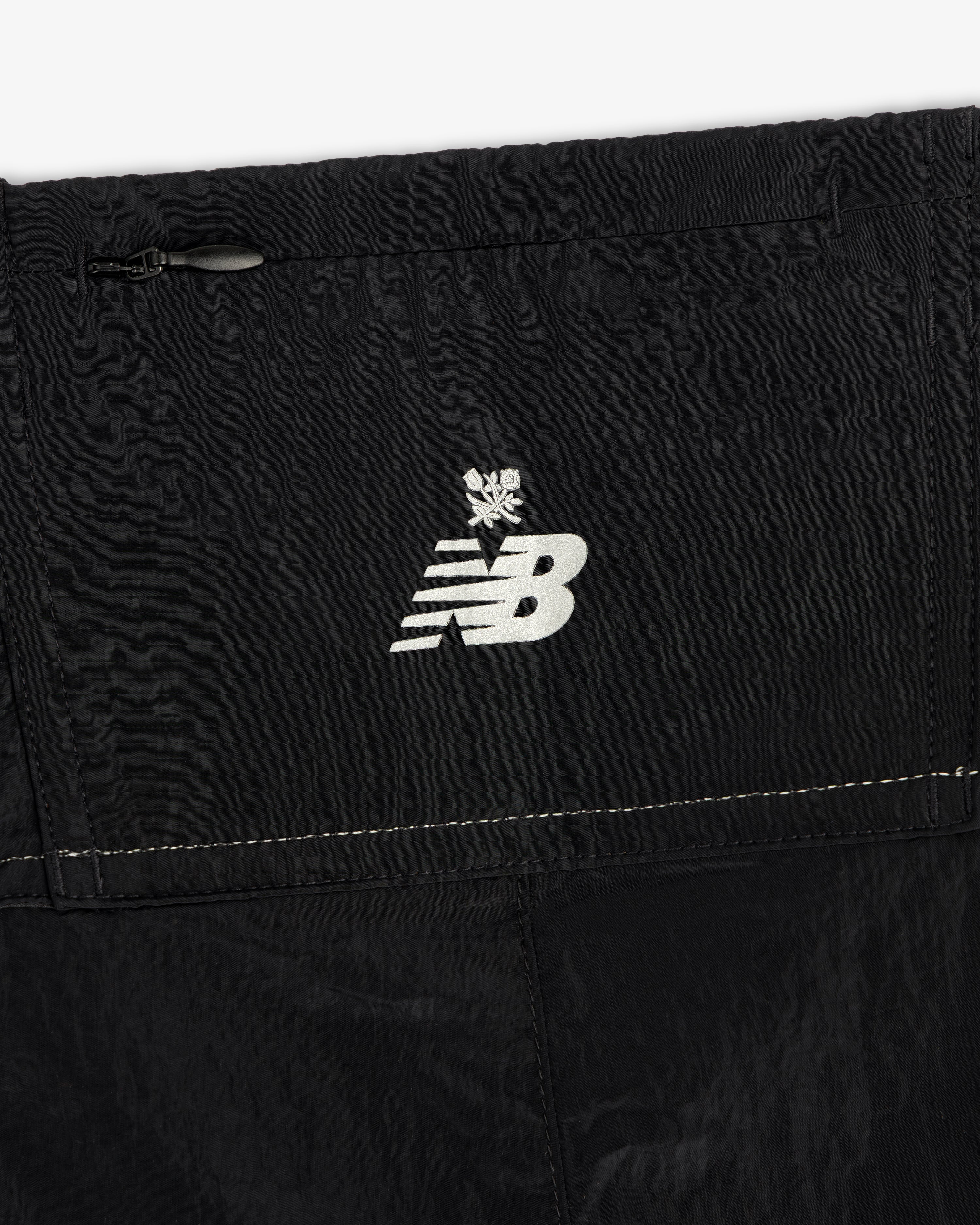 Close-up of black ALD / New Balance Lightweight Nylon Warmup Pant with a white logo and snowflake symbol above it.
