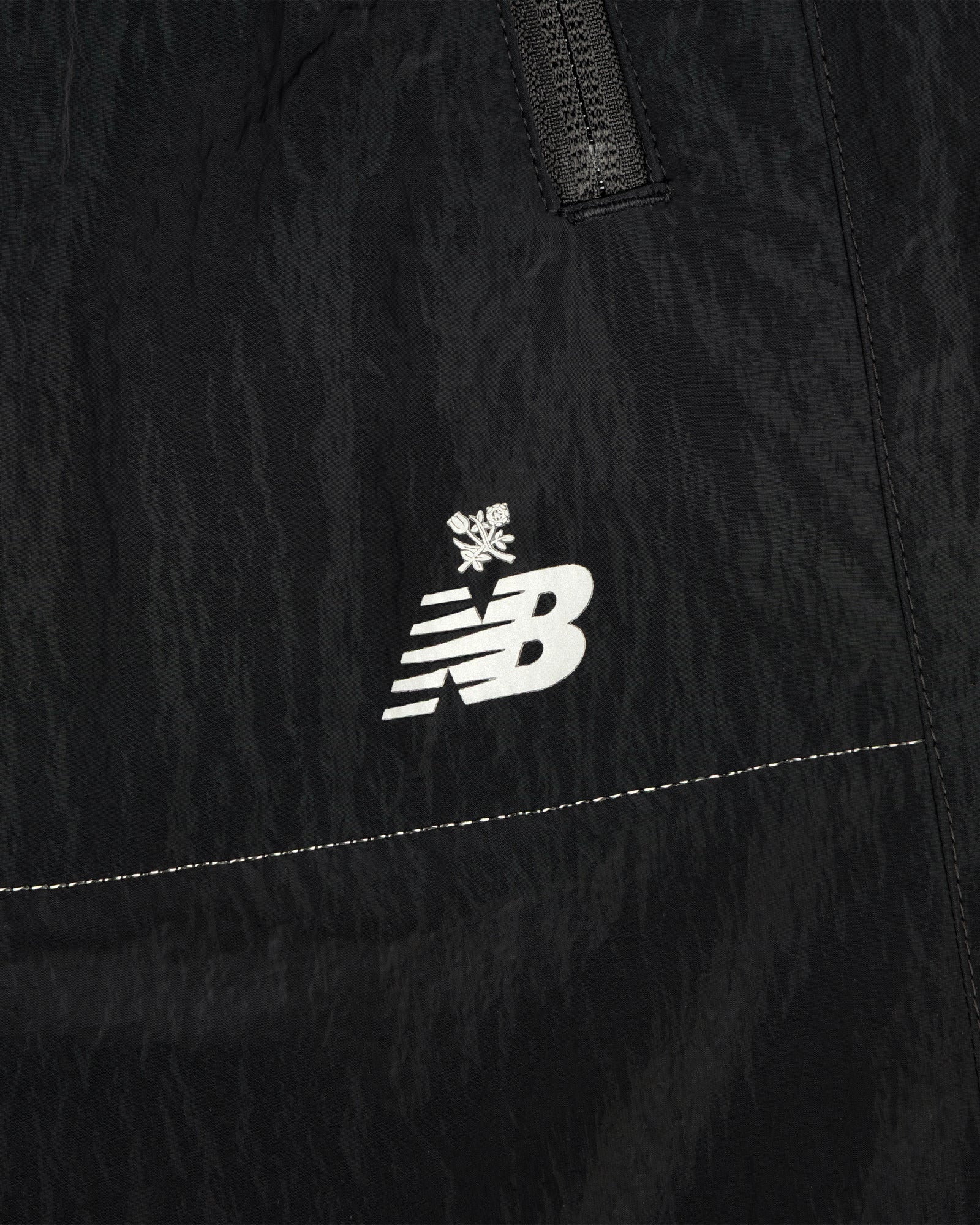 Close-up of ALD / New Balance Lightweight Nylon Warmup Pant in black, featuring a white logo with a small snowflake above it.