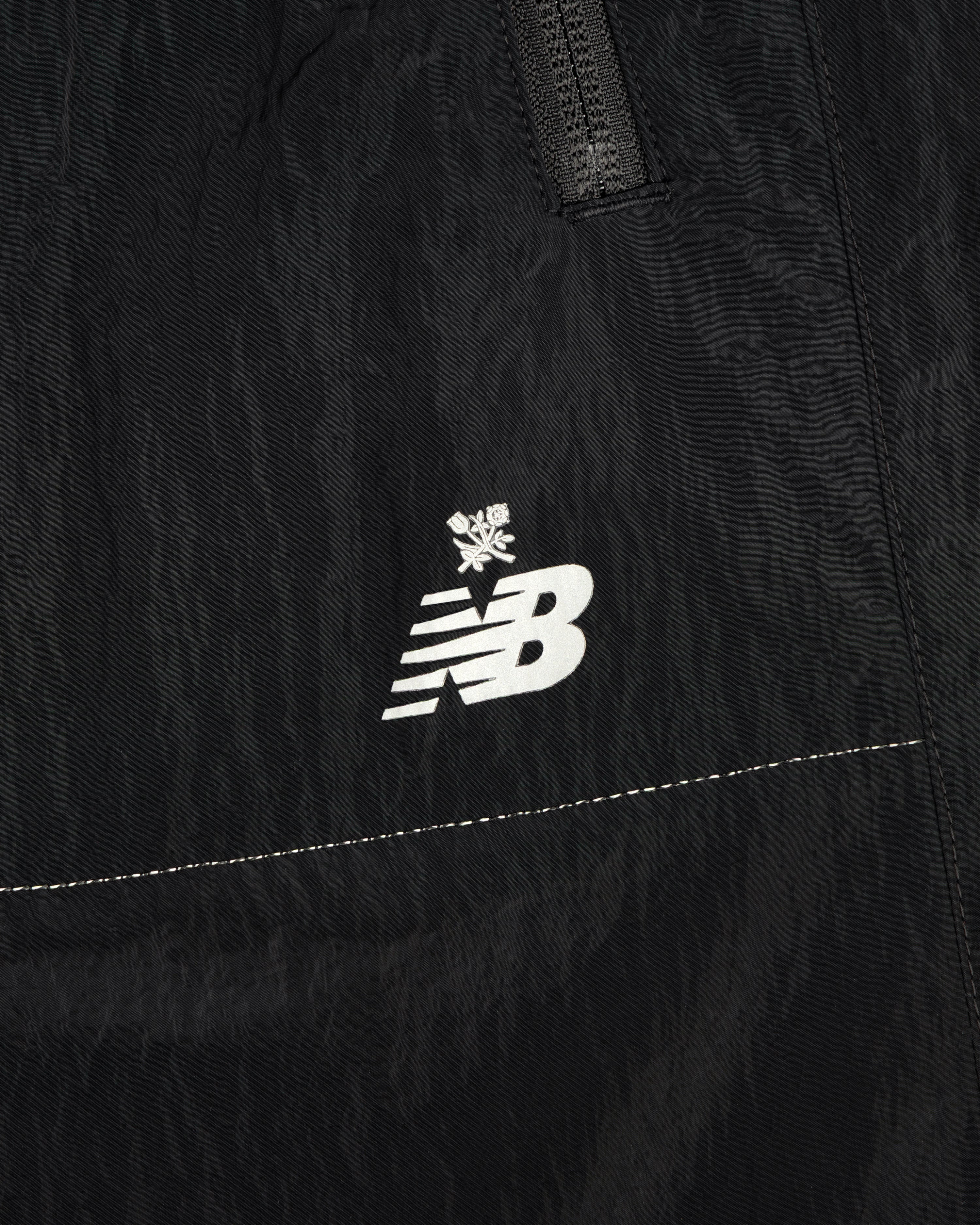 Close-up of ALD / New Balance Lightweight Nylon Warmup Pant in black, featuring a white logo with a small snowflake above it.