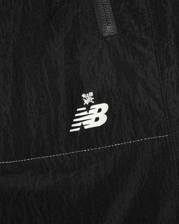 Close-up of ALD / New Balance Lightweight Nylon Warmup Pant in black, featuring a white logo with a small snowflake above it.