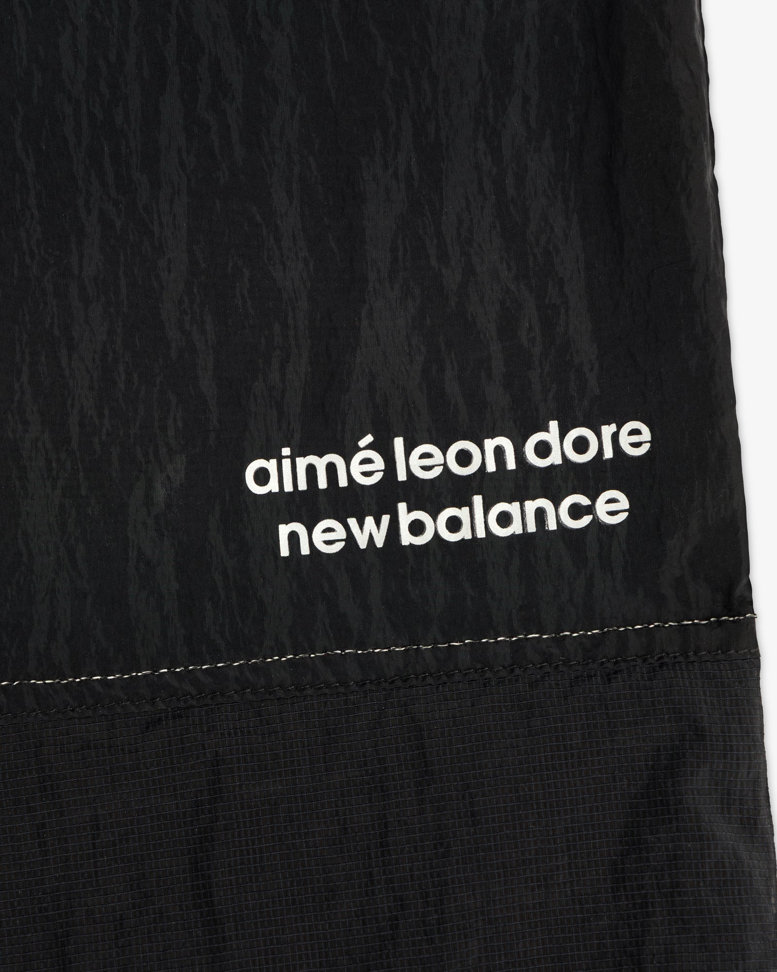 Close-up of black ALD / New Balance Lightweight Nylon Warmup Pant with white text printed near the seam.