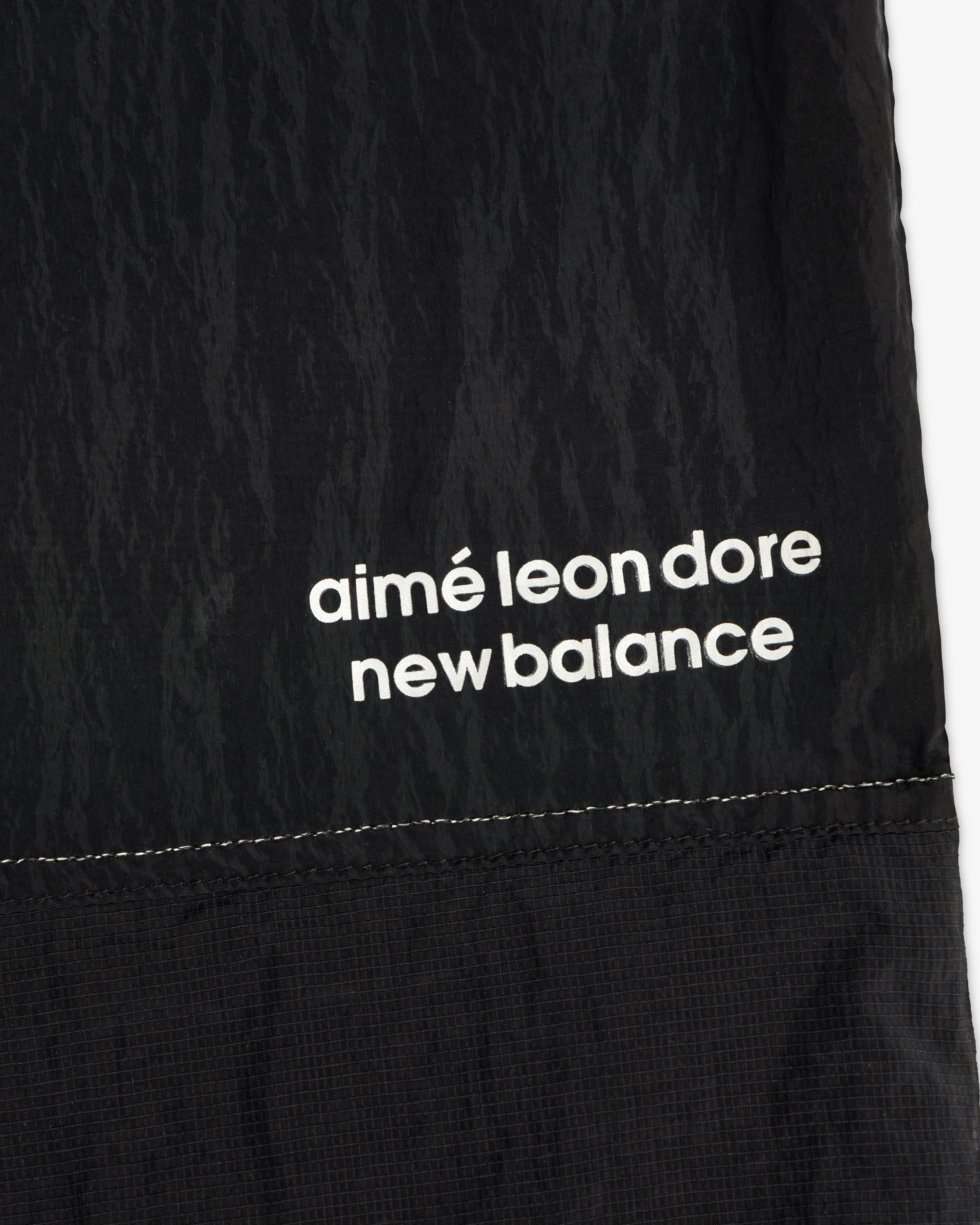 Close-up of black ALD / New Balance Lightweight Nylon Warmup Pant with white text printed near the seam.