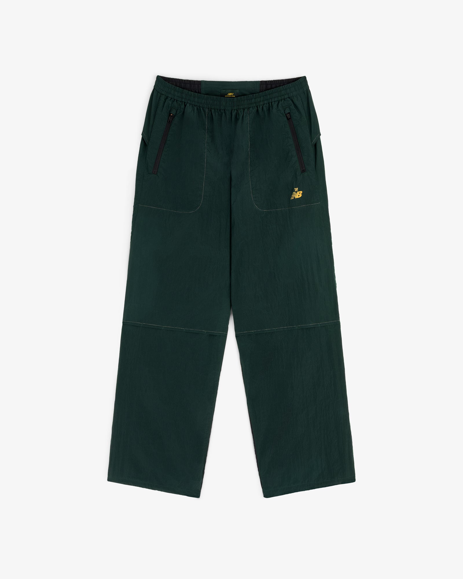 ALD / New Balance Lightweight Nylon Warmup Pant in dark green with front pockets, black zippers, and yellow logo.
