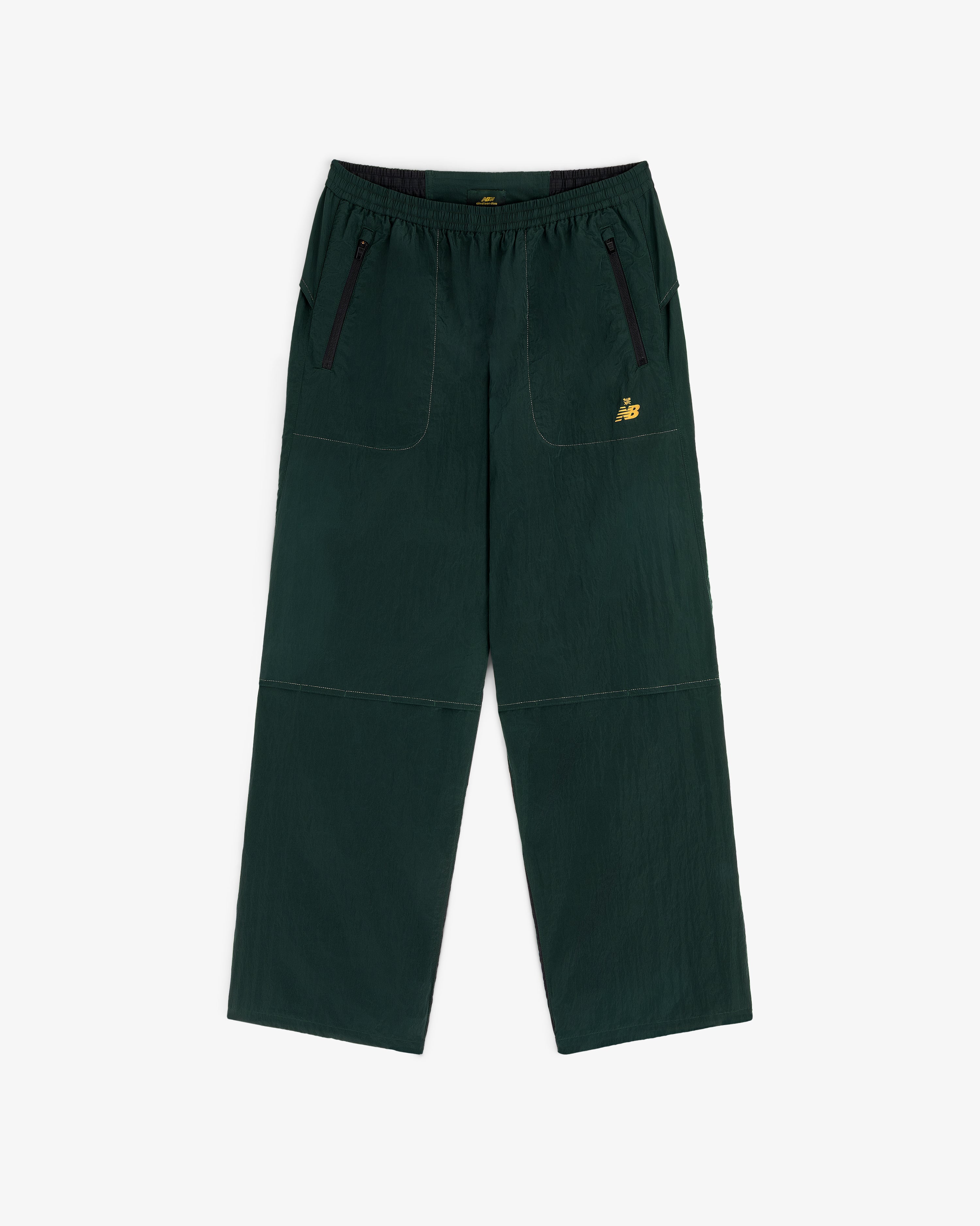 ALD / New Balance Lightweight Nylon Warmup Pant in dark green with front pockets, black zippers, and yellow logo.