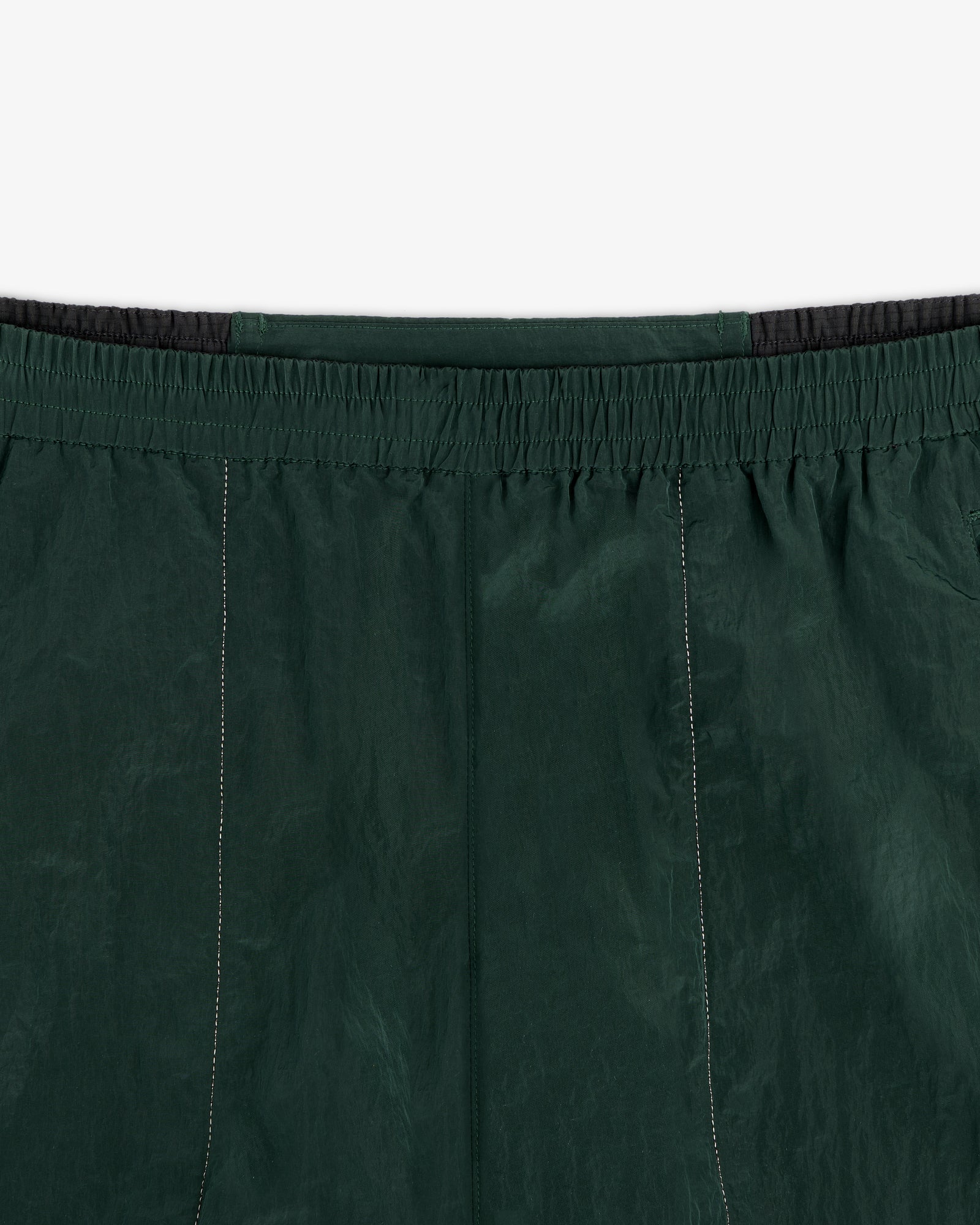 Close-up of ALD / New Balance Lightweight Nylon Warmup Pant in dark green with elastic waistband and stitching details.