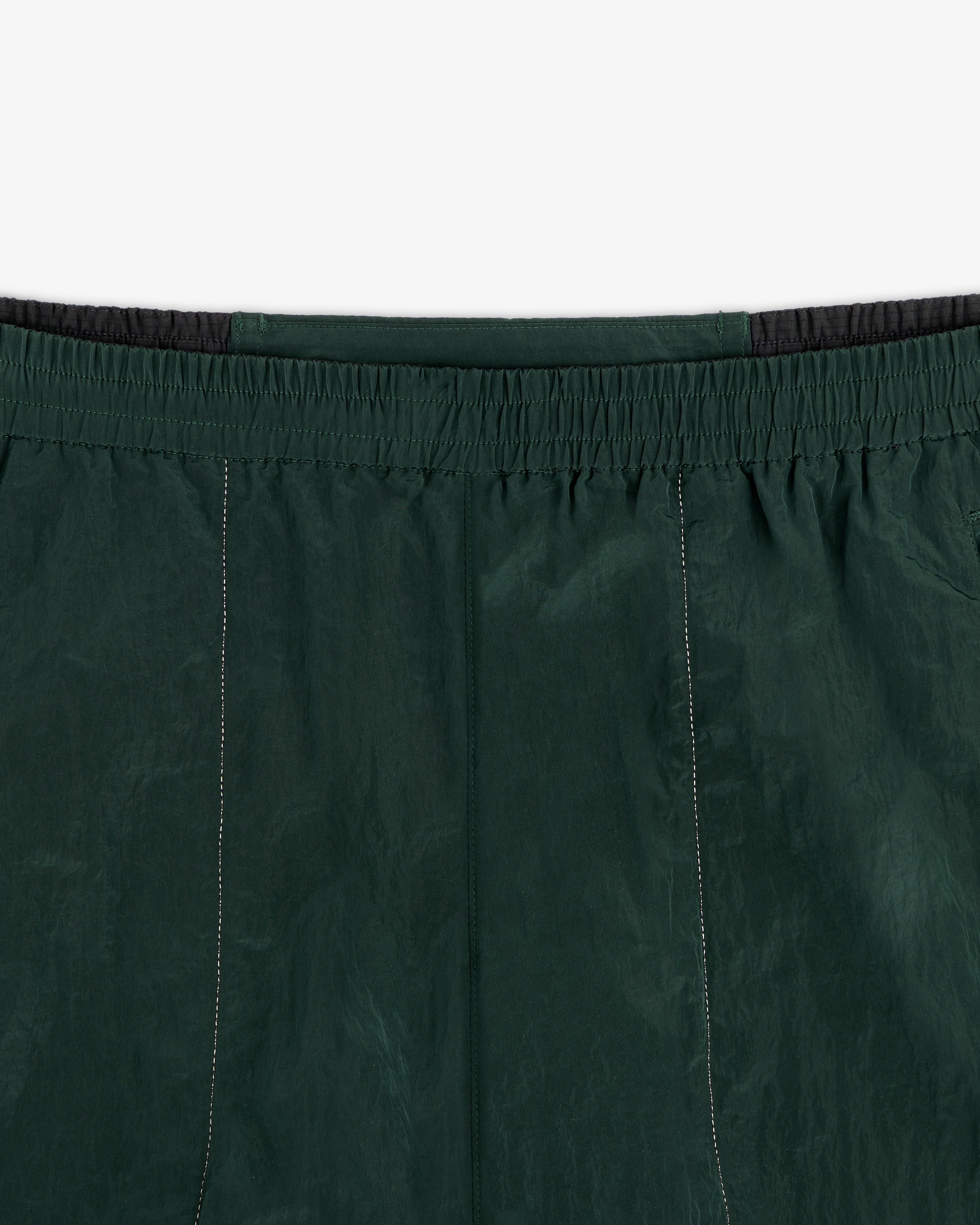 Close-up of ALD / New Balance Lightweight Nylon Warmup Pant in dark green with elastic waistband and stitching details.