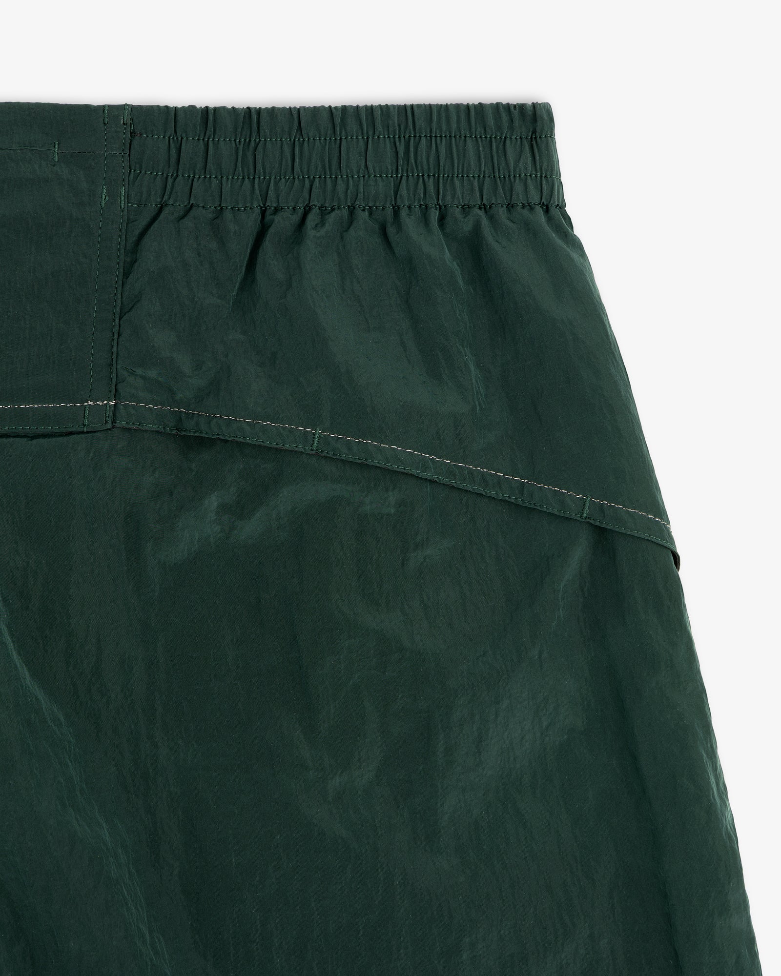 Close-up of the waistband and upper fabric of ALD / New Balance Lightweight Nylon Warmup Pant in dark green.