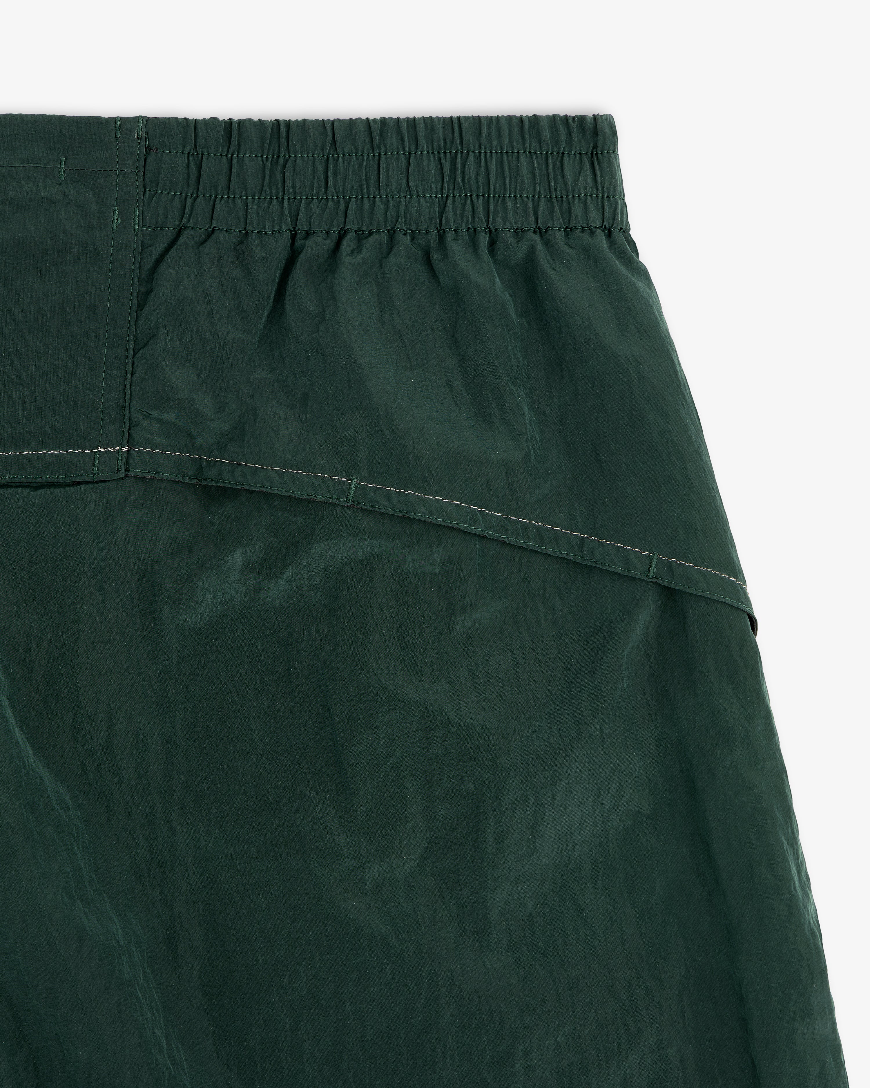 Close-up of the waistband and upper fabric of ALD / New Balance Lightweight Nylon Warmup Pant in dark green.