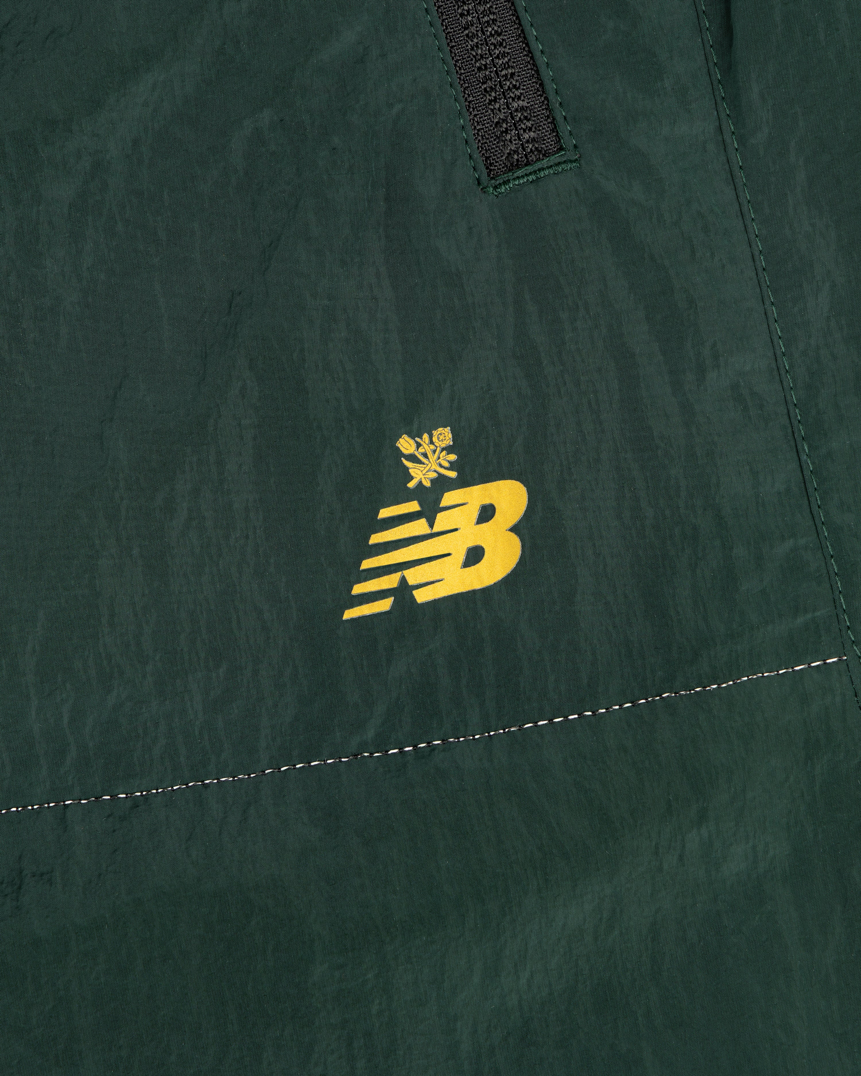 Close-up of green ALD / New Balance Lightweight Nylon Warmup Pant with a yellow logo topped by a small crown.
