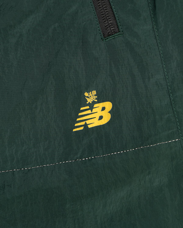 Close-up of green ALD / New Balance Lightweight Nylon Warmup Pant with a yellow logo topped by a small crown.