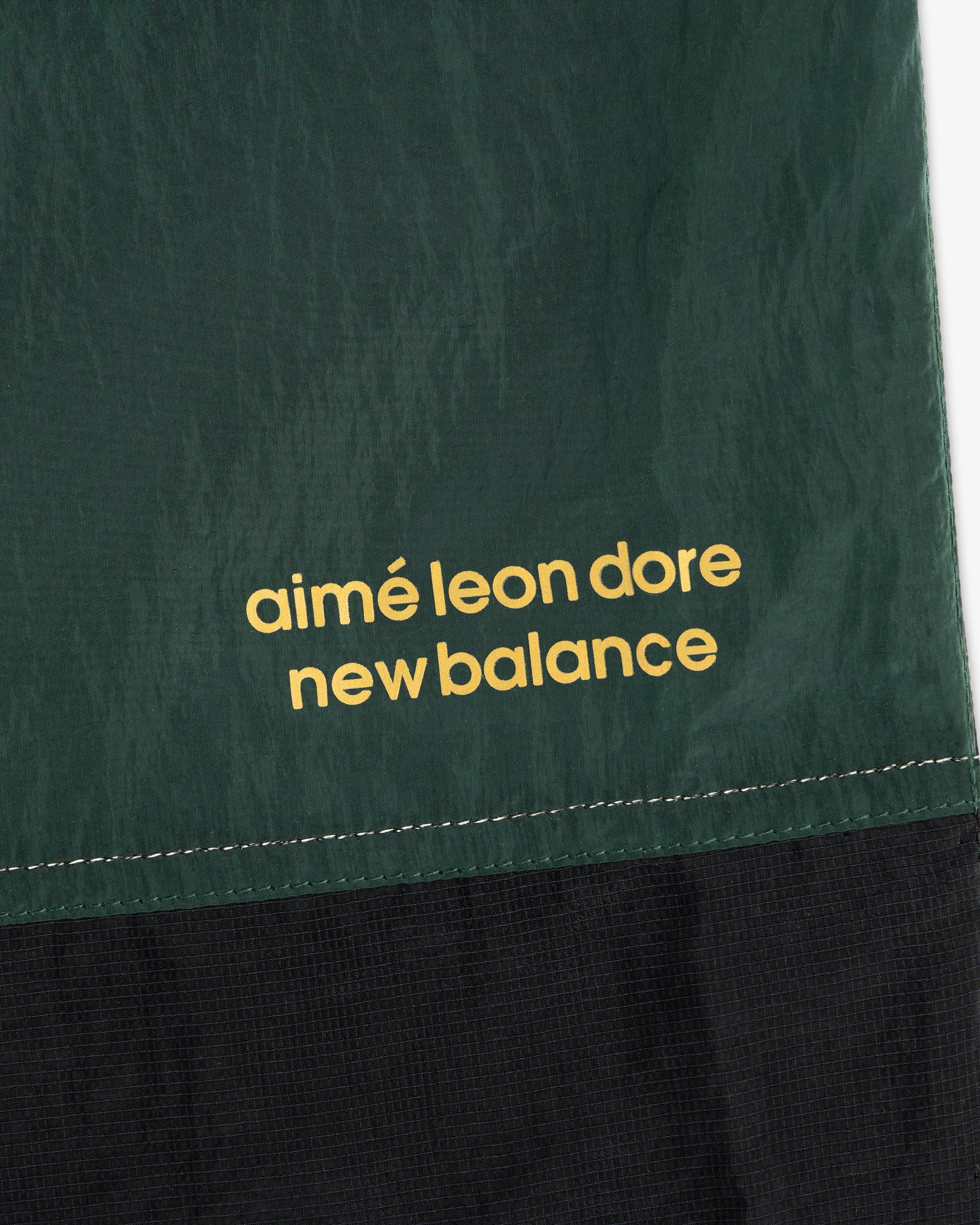 Close-up of green and black ALD / New Balance Lightweight Nylon Warmup Pant with yellow printed text.