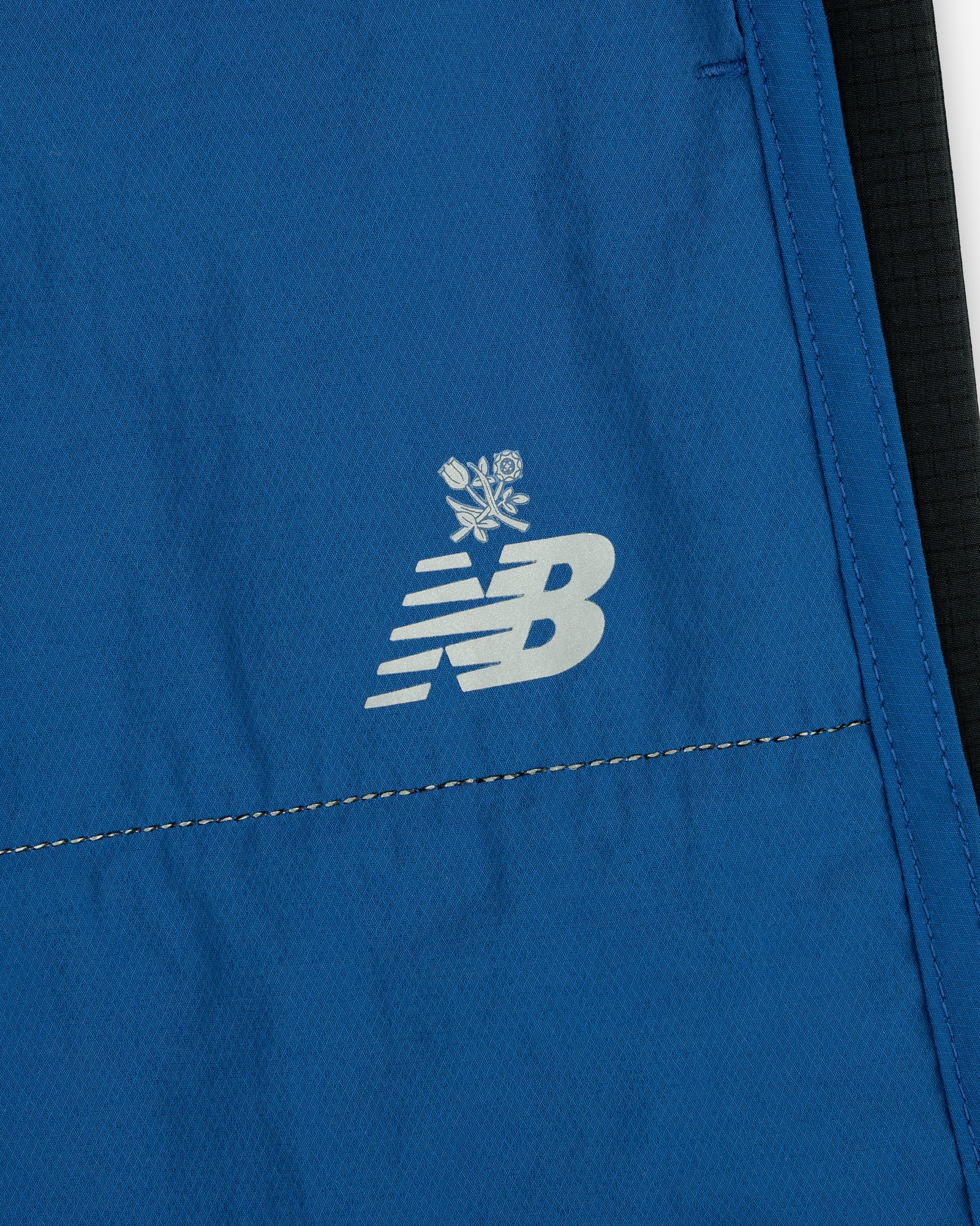 ALD / New Balance Performance Lightweight Running Short in blue, featuring a white NB logo and small crossed rose icons.
