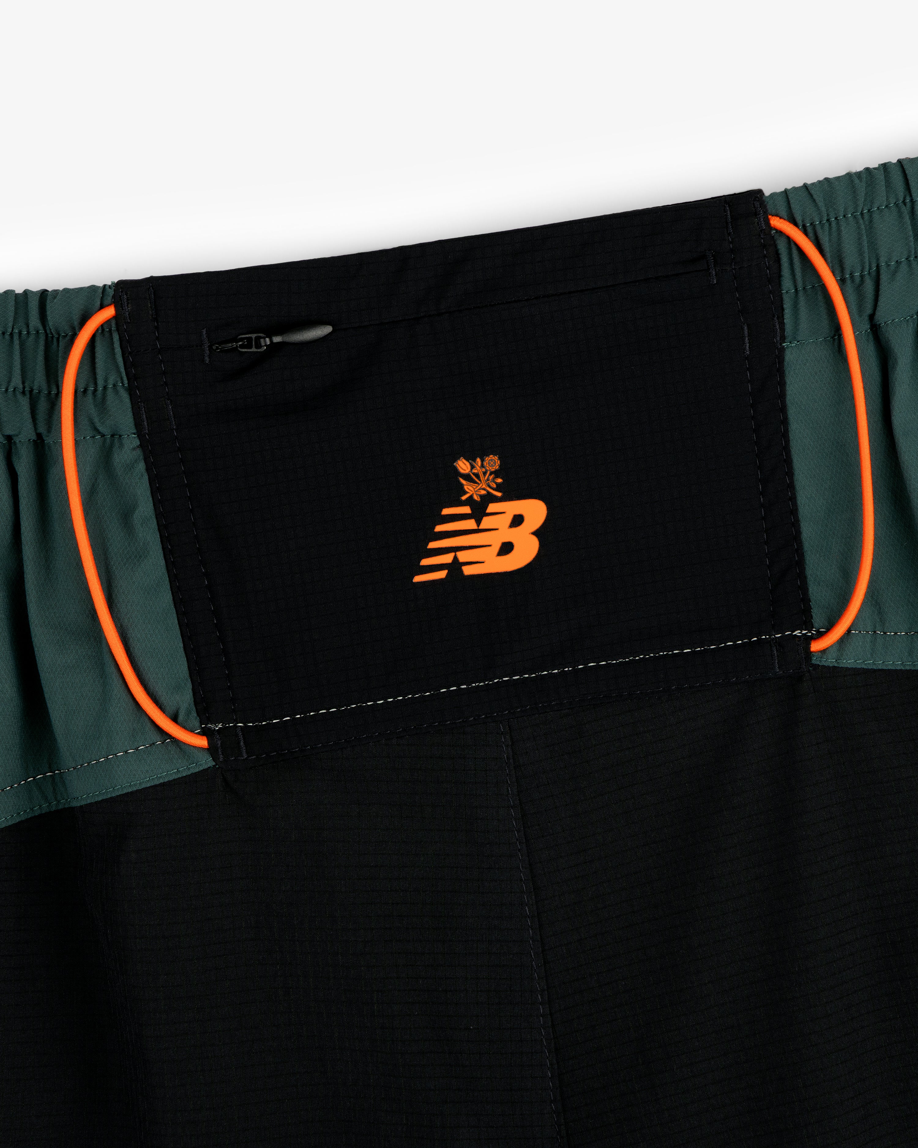 Close-up of ALD / New Balance Performance Lightweight Running Short in black with orange logo and green side panels.