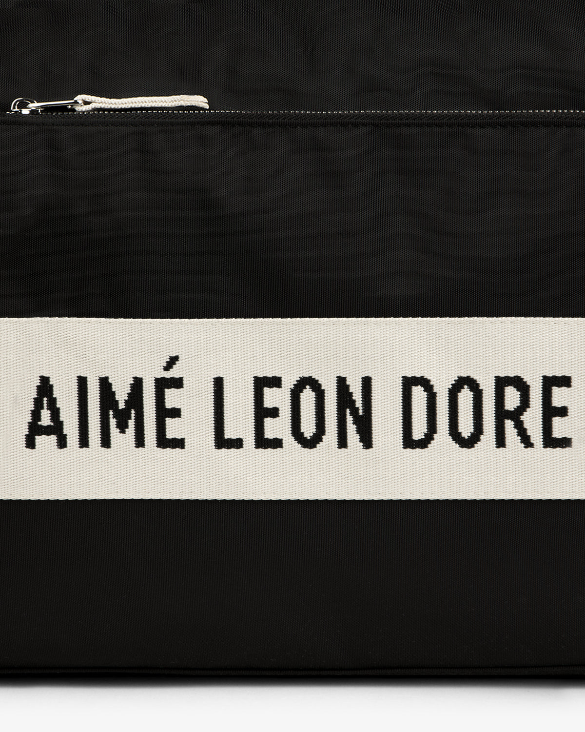 Black nylon duffle bag with a white stripe featuring "AIMÉ LEON DORE" text in bold black letters.