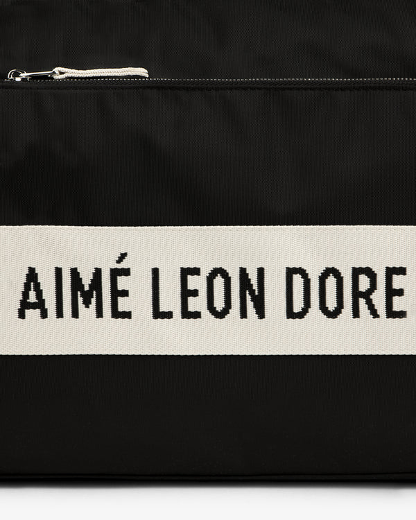 Black nylon duffle bag with a white stripe featuring "AIMÉ LEON DORE" text in bold black letters.