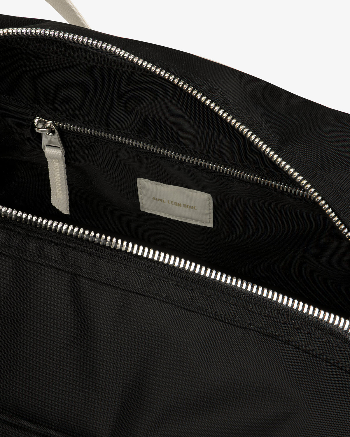 Close-up of an open Nylon Duffle Bag in black with a silver zipper, inside pocket, and white label.