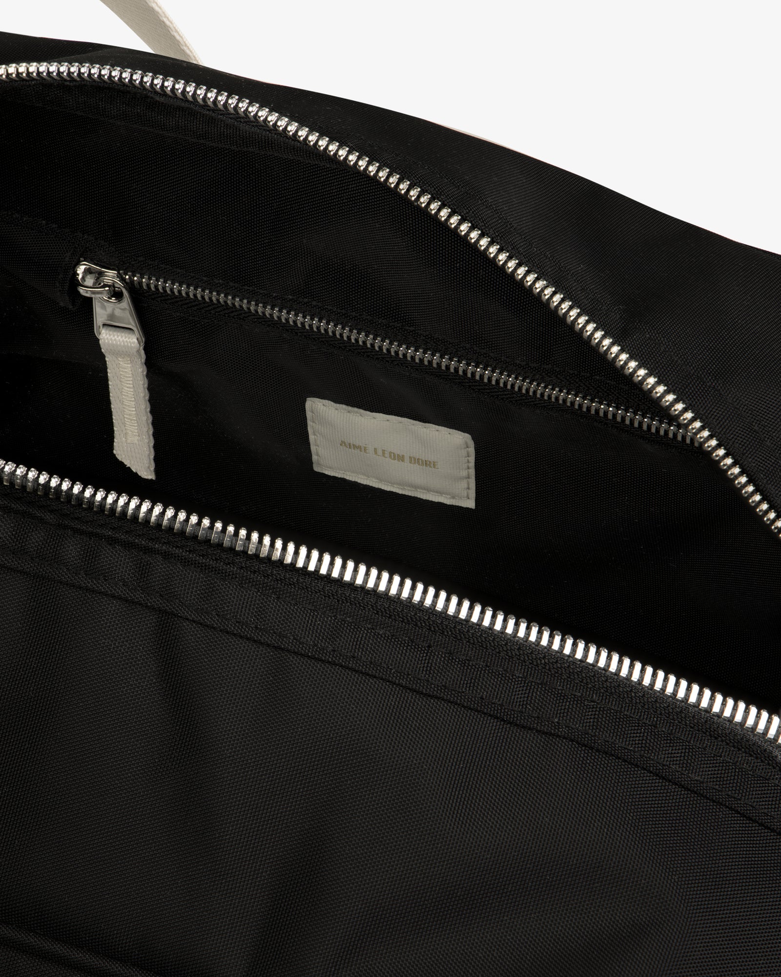 Close-up of an open Nylon Duffle Bag in black with a silver zipper, inside pocket, and white label.