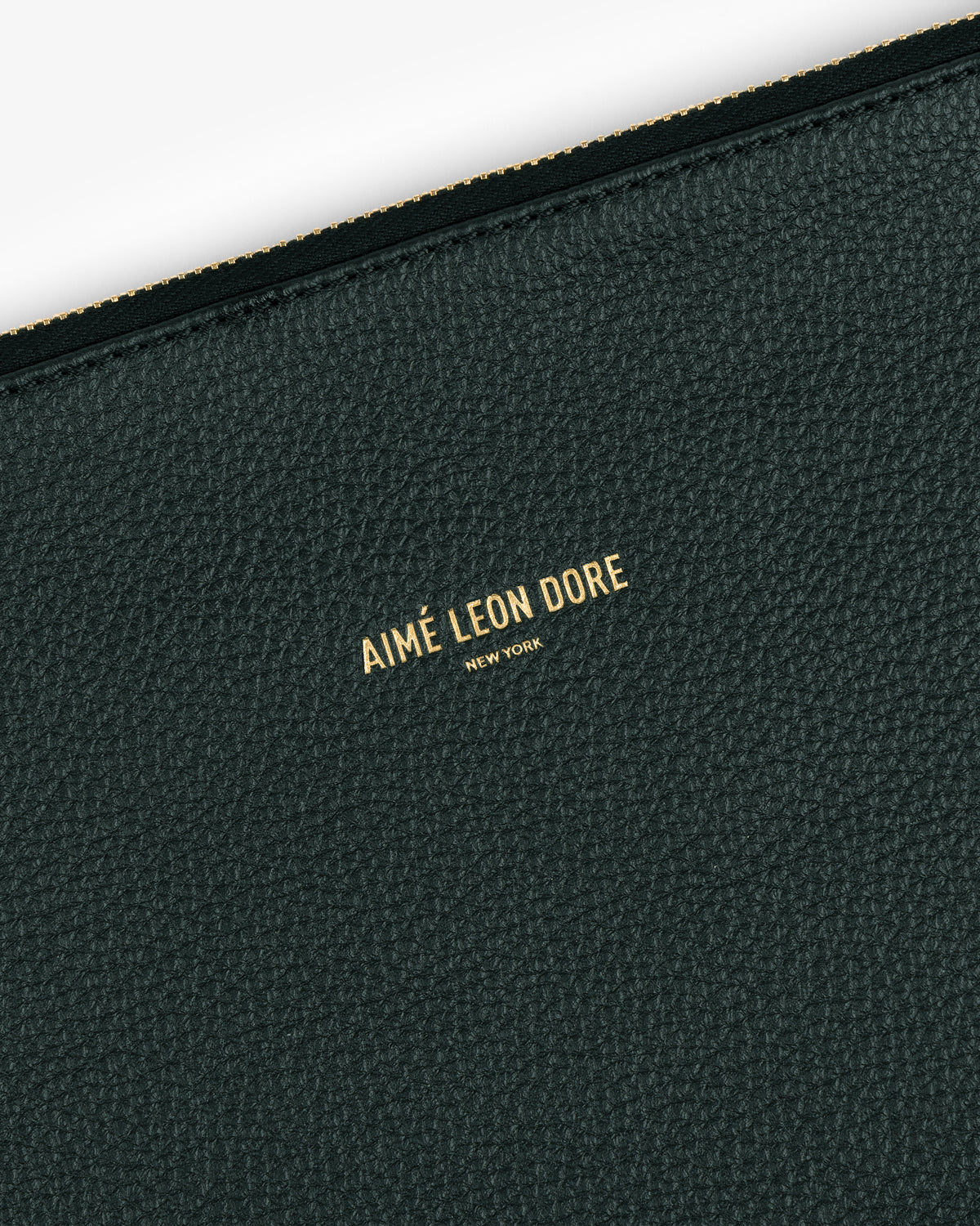 Close-up of a dark green Small Leather Pouch with AIMÉ LEON DORE NEW YORK embossed in gold letters.