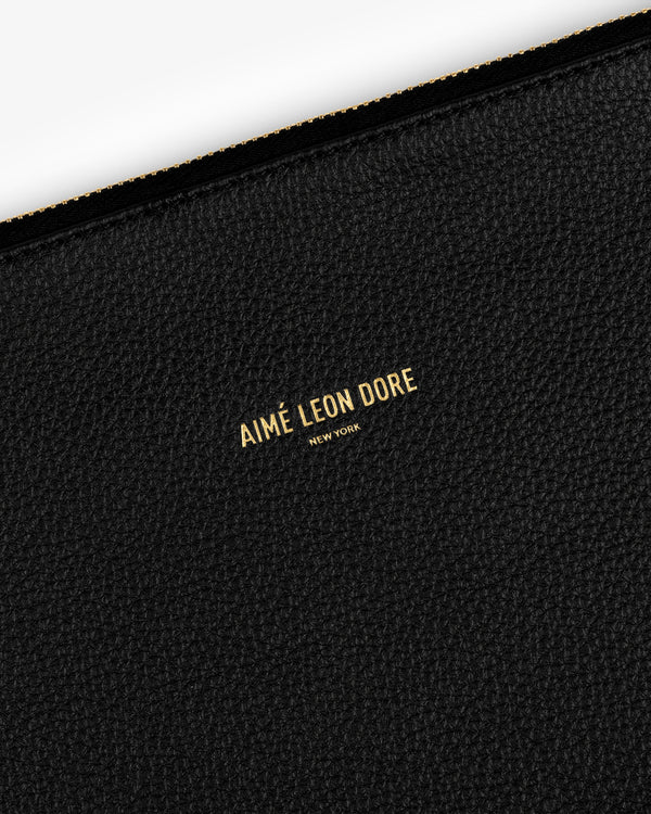 Close-up of a black textured Small Leather Pouch with AIMÉ LEON DORE NEW YORK embossed in gold text.