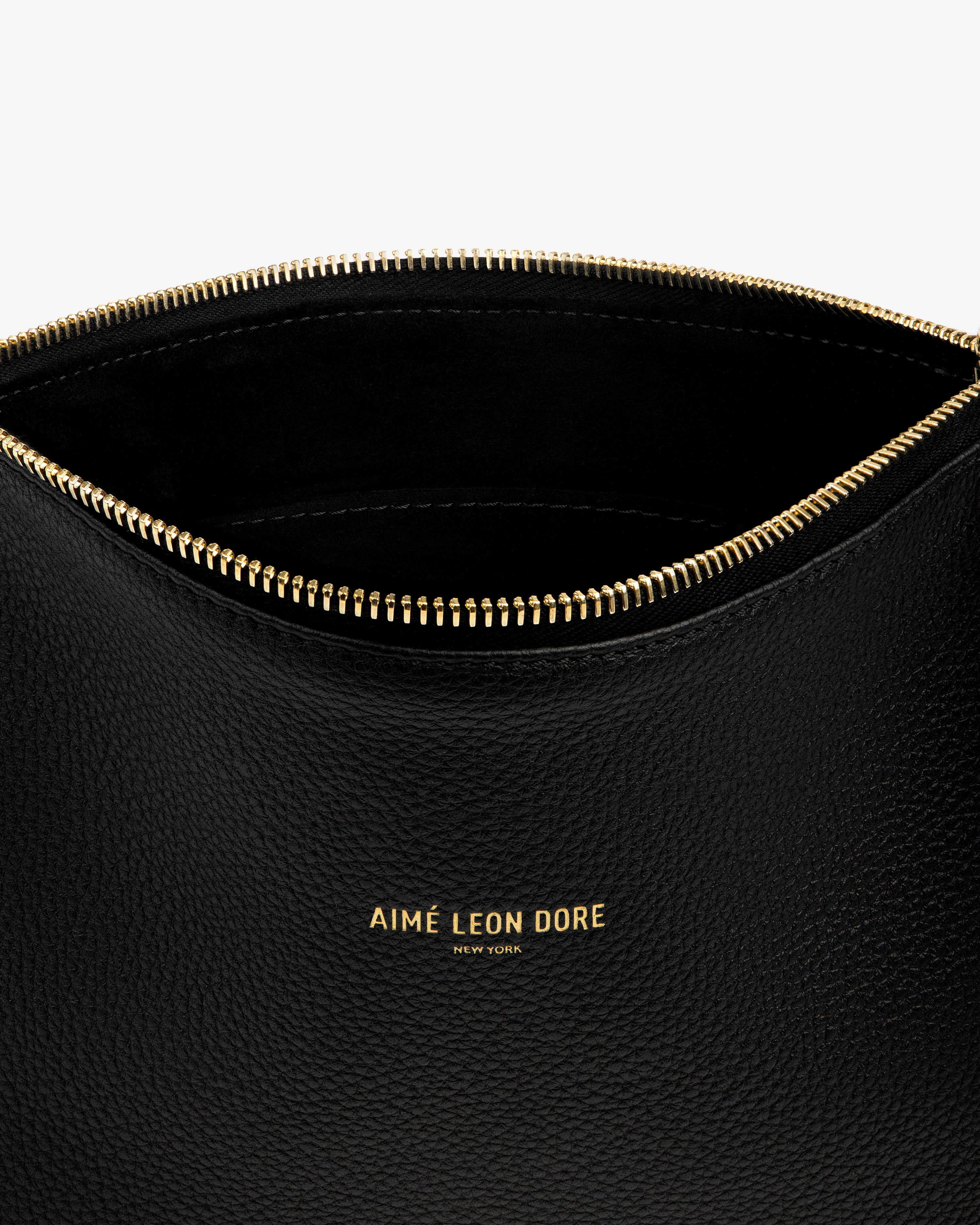 Close-up of the Small Leather Pouch—open, black leather with a gold zipper and AIMÉ LEON DORE NEW YORK in gold.