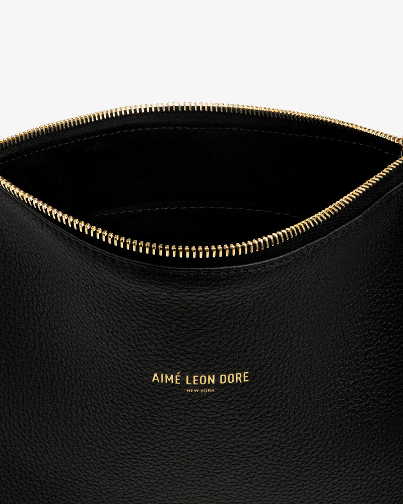 Close-up of the Small Leather Pouch—open, black leather with a gold zipper and AIMÉ LEON DORE NEW YORK in gold.
