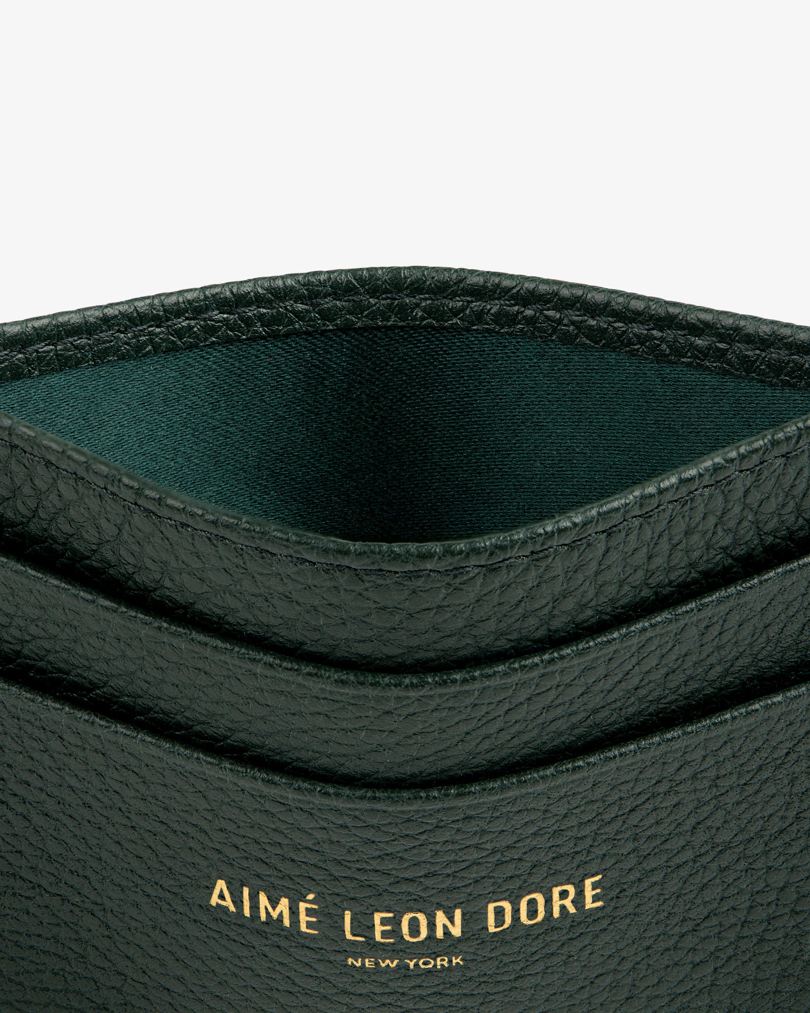Close-up of a dark green Leather Card Holder with AIMÉ LEON DORE NEW YORK stamped in gold letters.
