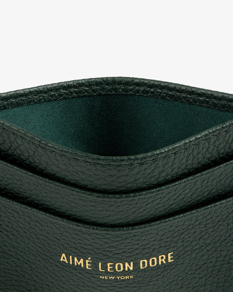 Close-up of a dark green Leather Card Holder with AIMÉ LEON DORE NEW YORK stamped in gold letters.