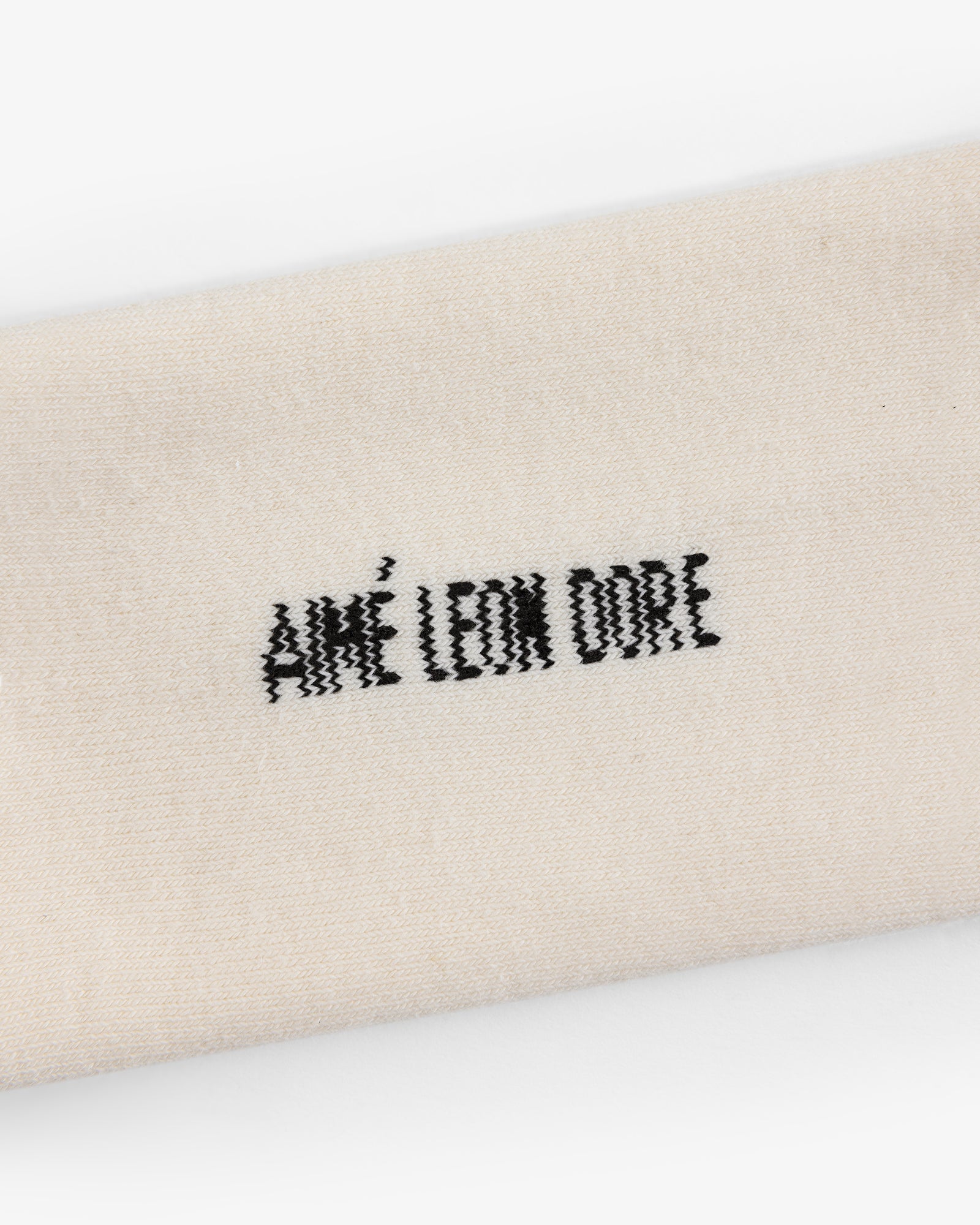 Close-up of cream-colored Crew Sock 3-Pack with AIMÉ LEON DORE embroidered in black thread.