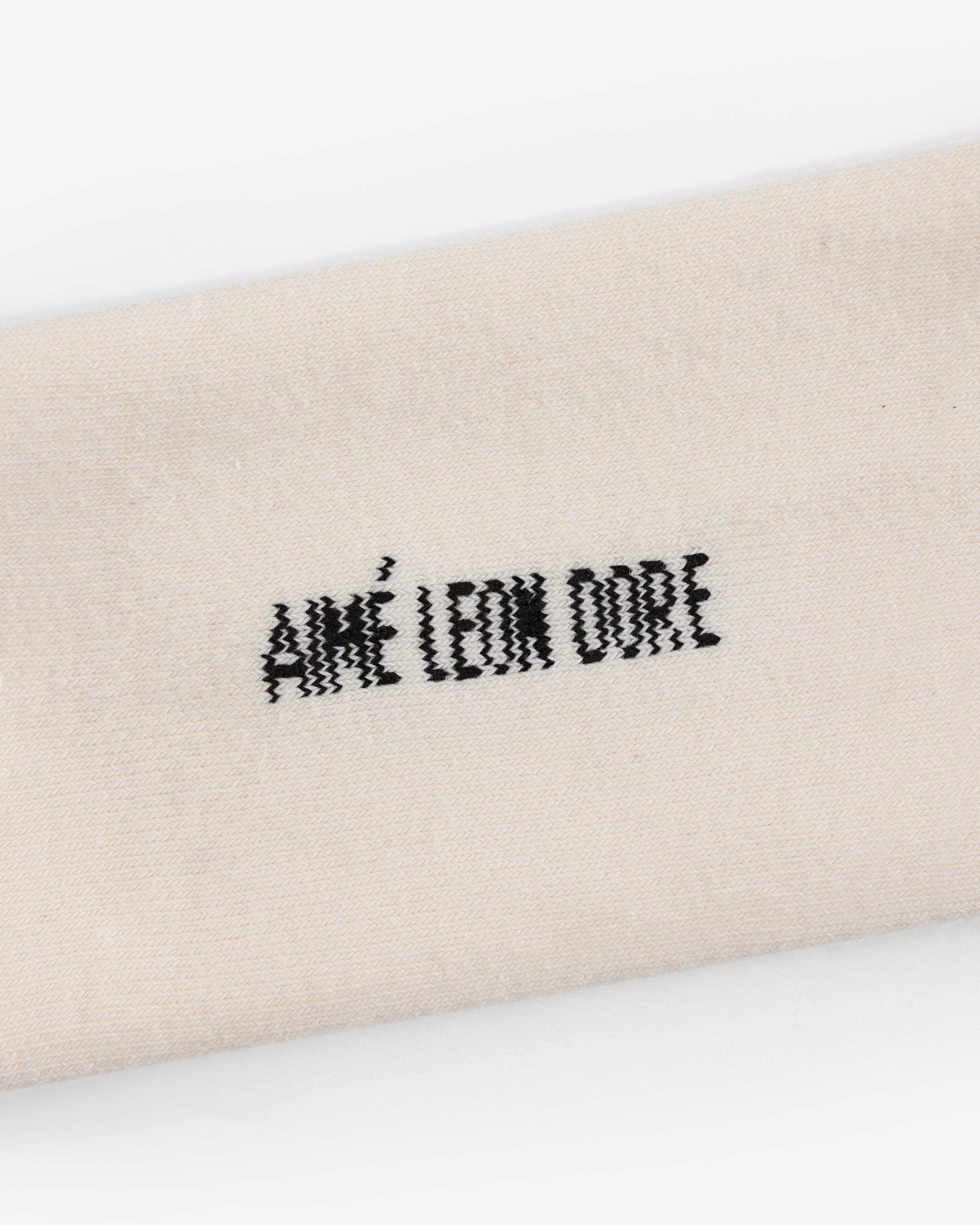 Close-up of cream-colored Crew Sock 3-Pack with AIMÉ LEON DORE embroidered in black thread.