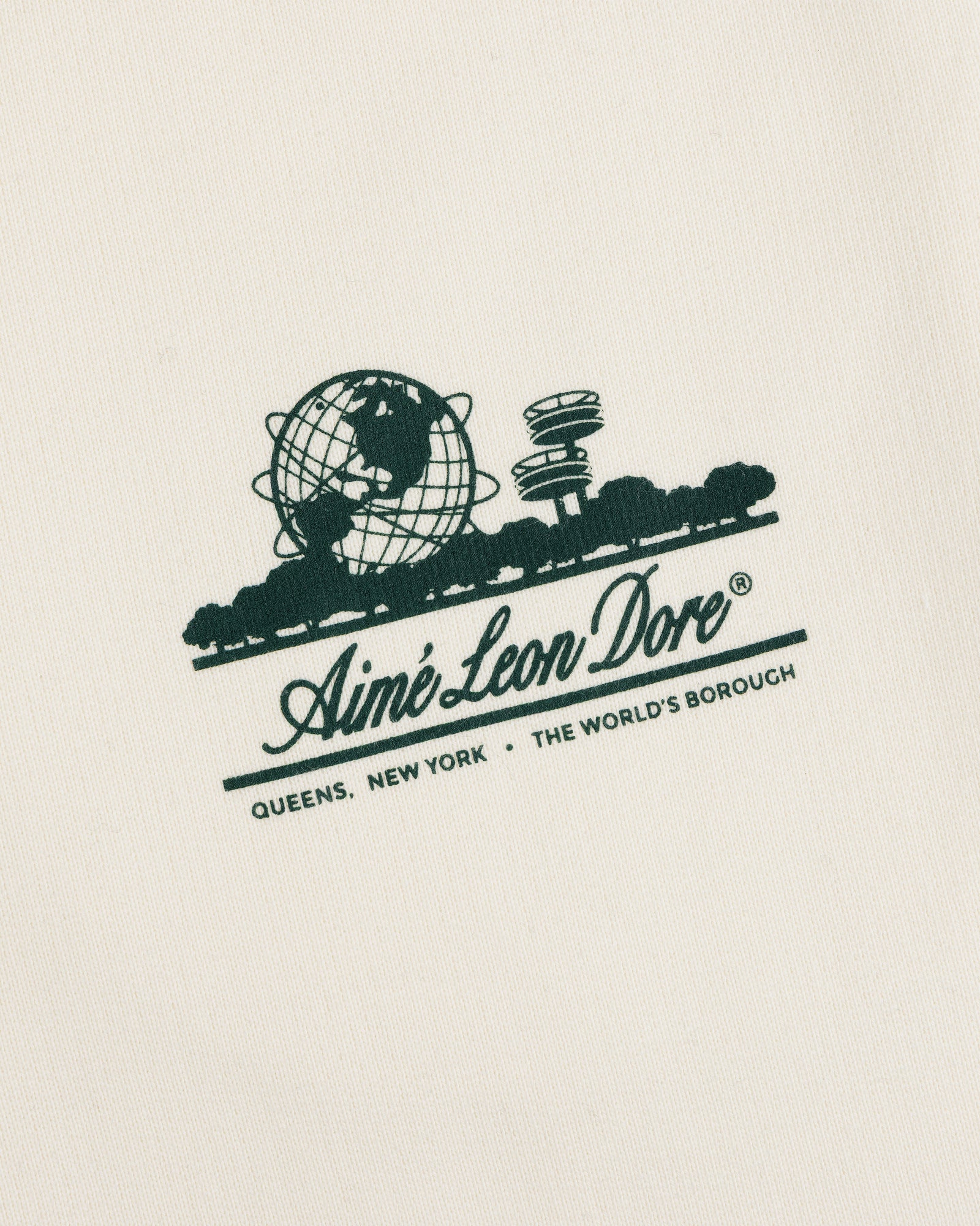 Unisphere Sweatpants feature a green Aimé Leon Dore logo and "QUEENS, NEW YORK - THE WORLDS BOROUGH" on cream fabric.