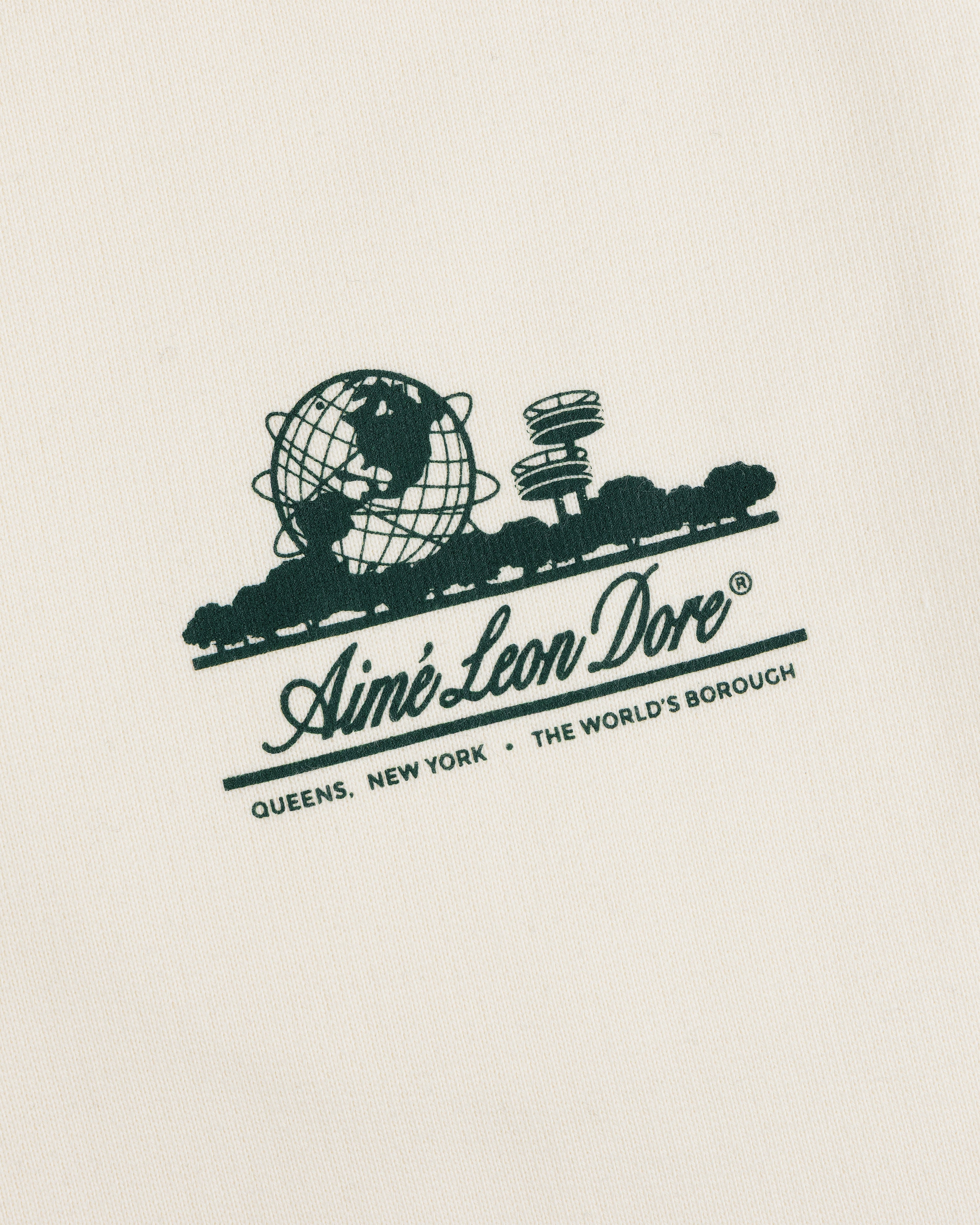 Unisphere Sweatpants feature a green Aimé Leon Dore logo and "QUEENS, NEW YORK - THE WORLDS BOROUGH" on cream fabric.