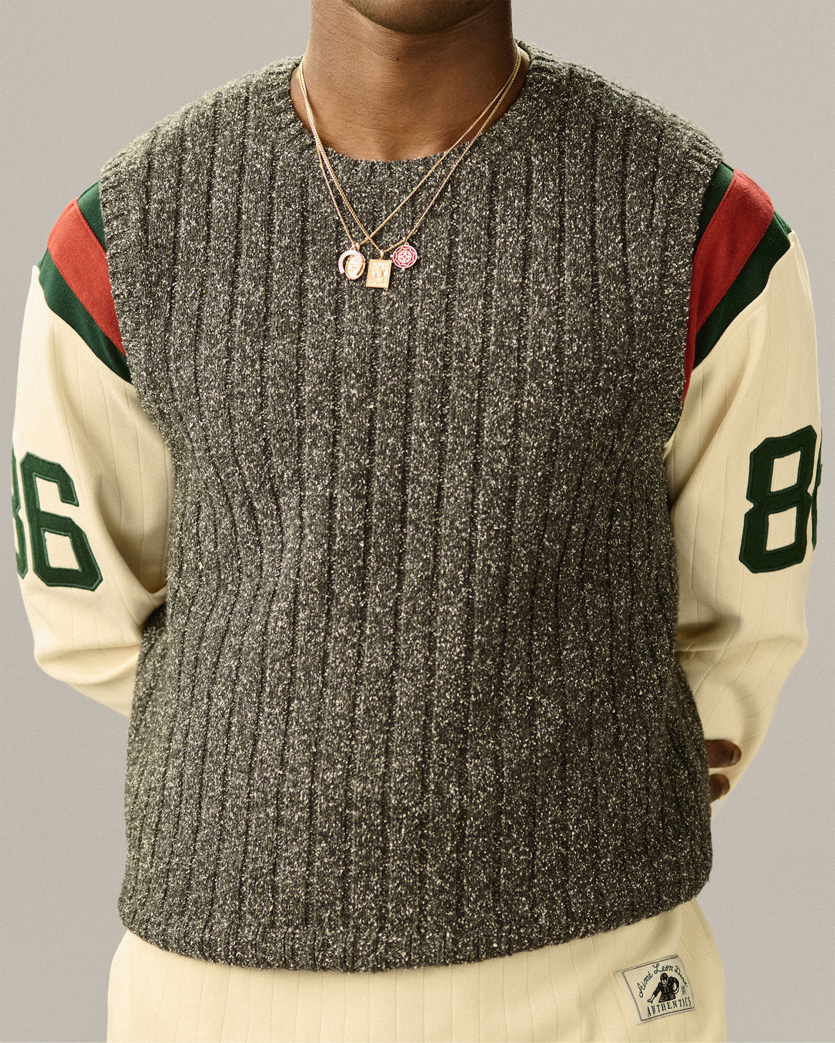Person in a grey vest and cream striped top, accessorized with the 14Kt Gold Rose Pendant and layered necklaces.