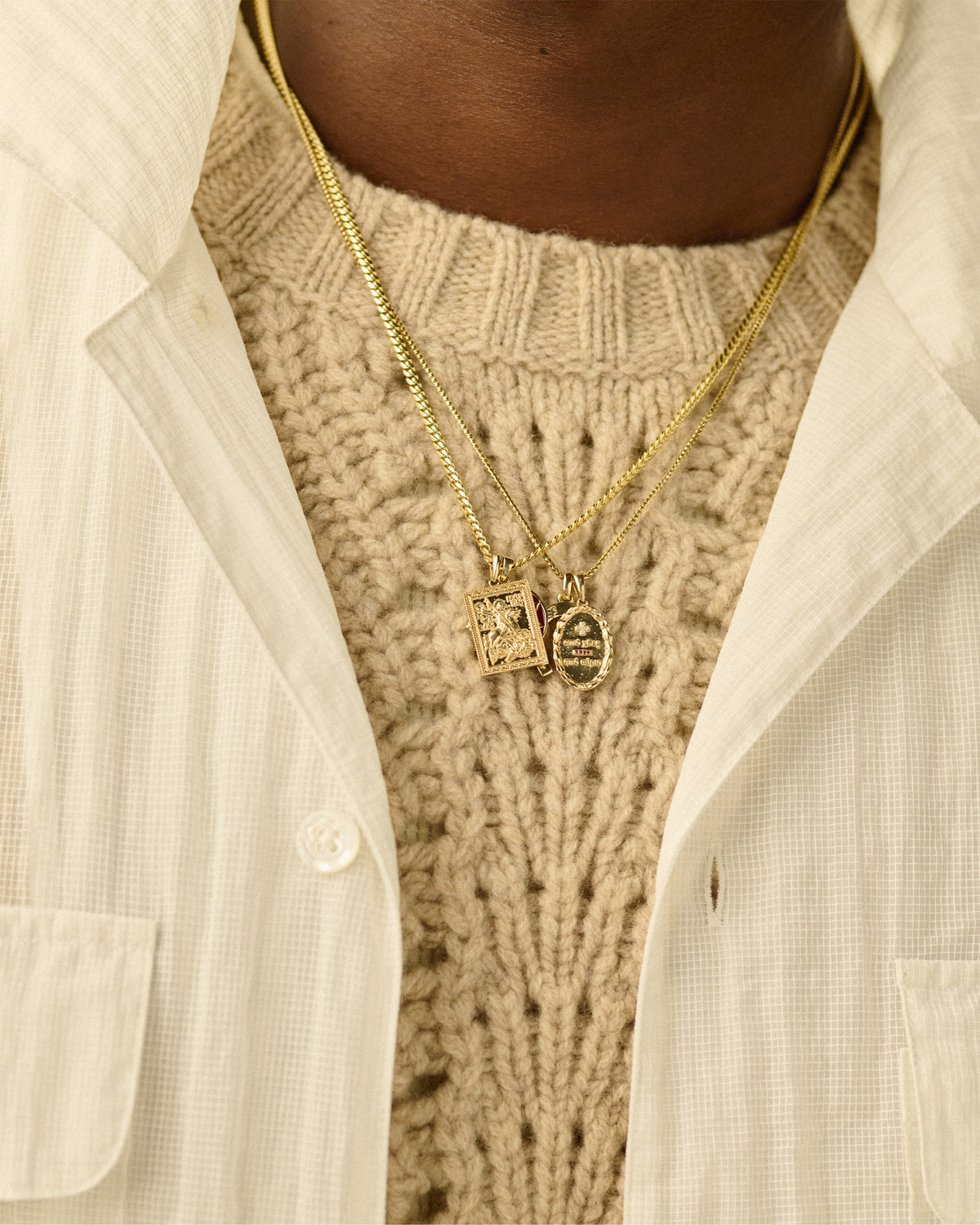 Close-up of a person wearing a 14Kt Gold Saint George Pendant over a beige knit sweater and off-white collared shirt.