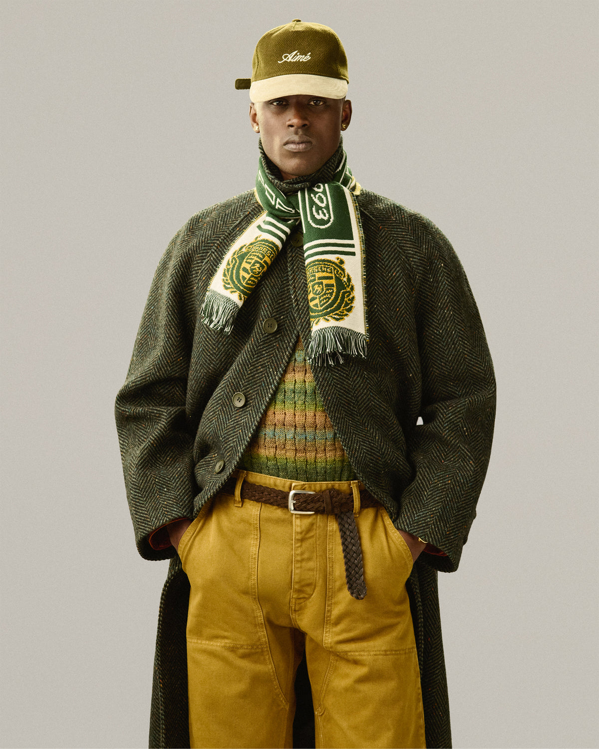 A man, hands in pockets, wears a green coat and a Braided Suede Belt, facing forward.