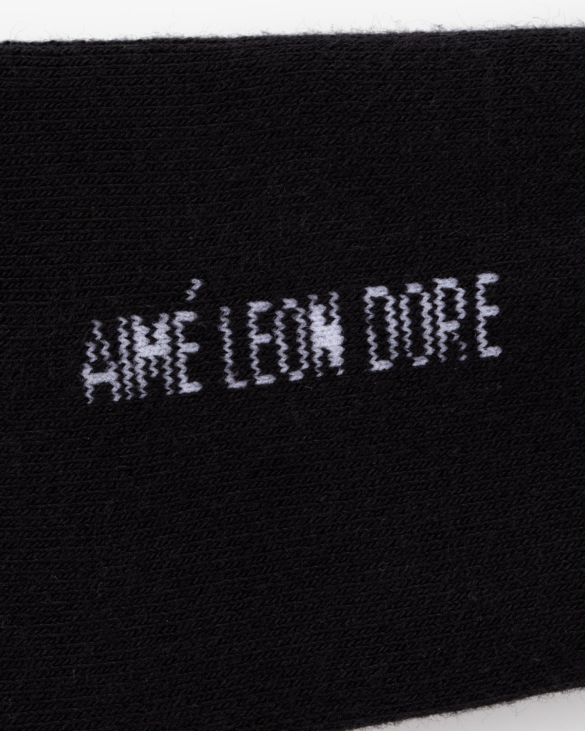 Black fabric with white, slightly distorted AIMÉ LEON DORE text woven in the center on Crew Sock 3-Pack.