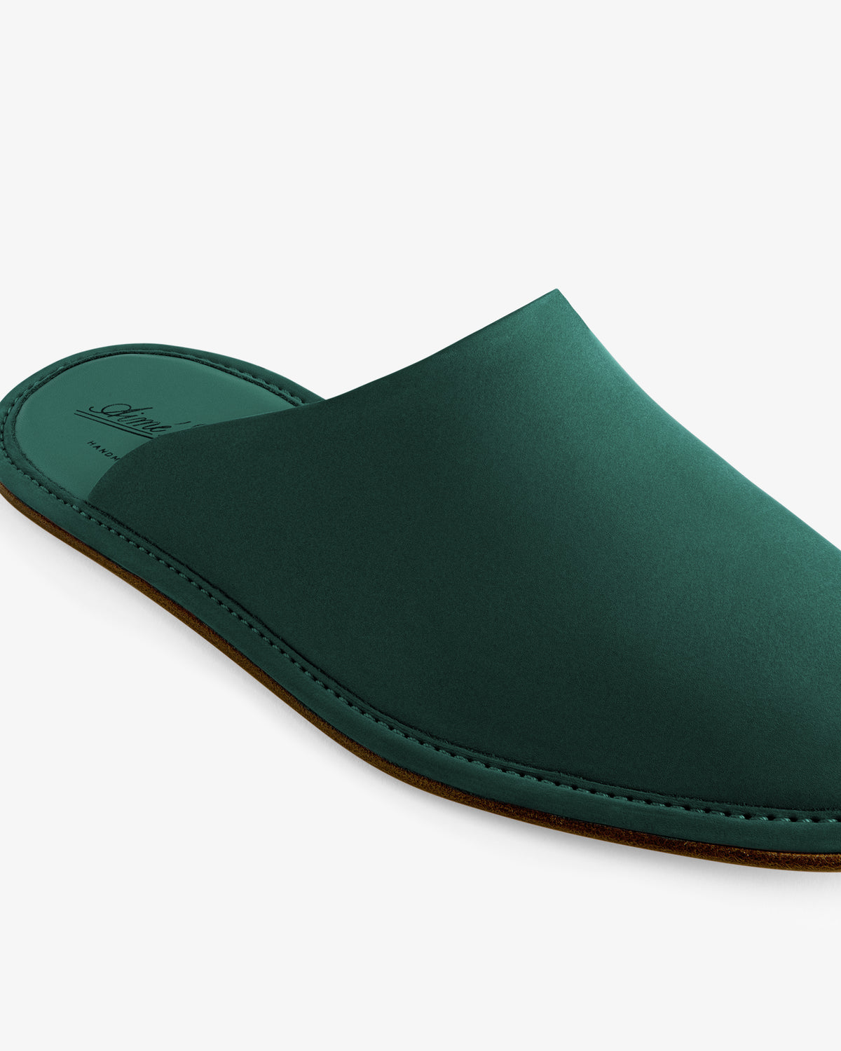 The Nubuck Travel Slipper is a dark green, closed-toe leather slipper with a flat brown sole on a white background.