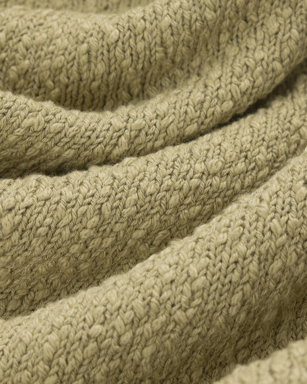 Close-up of textured, light olive green Nautical Rollneck Sweater with visible stitches and gentle folds.