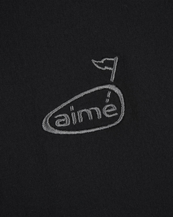 ALD Golf Cordura Tips Jacket: Gray aimé logo with flag above the e, embroidered on black fabric.