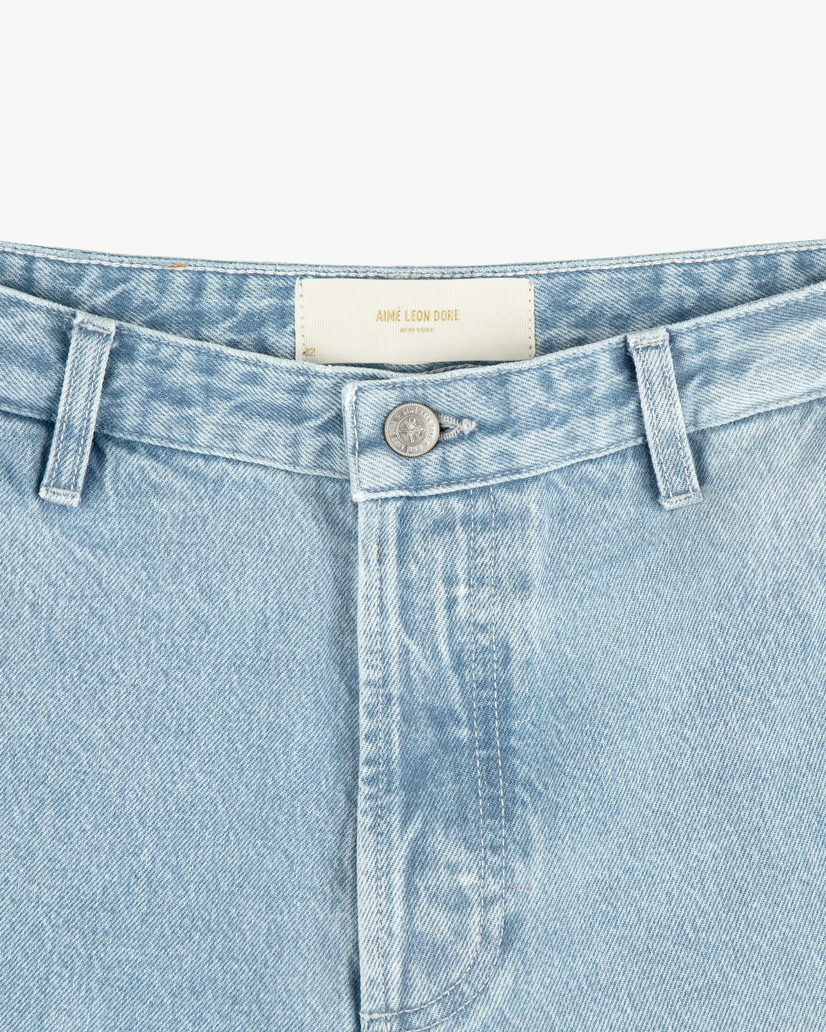 Close-up of light blue Denim Carpenter Pant with a silver button and visible AIME LEON DORE label on the waistband.