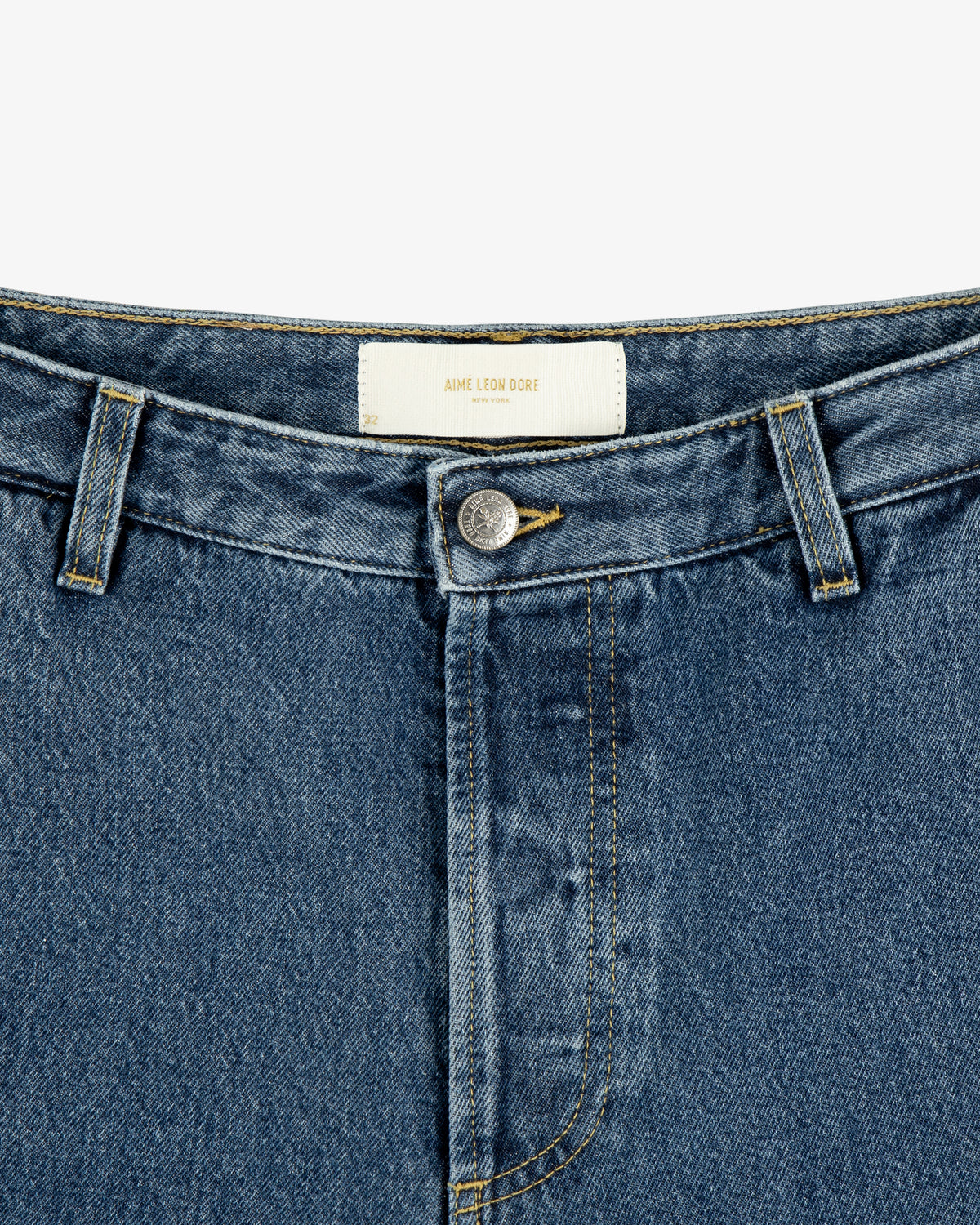 Close-up of Denim Carpenter Pant in blue with a button, belt loops, and a white Aimé Leon Dore label on the waistband.