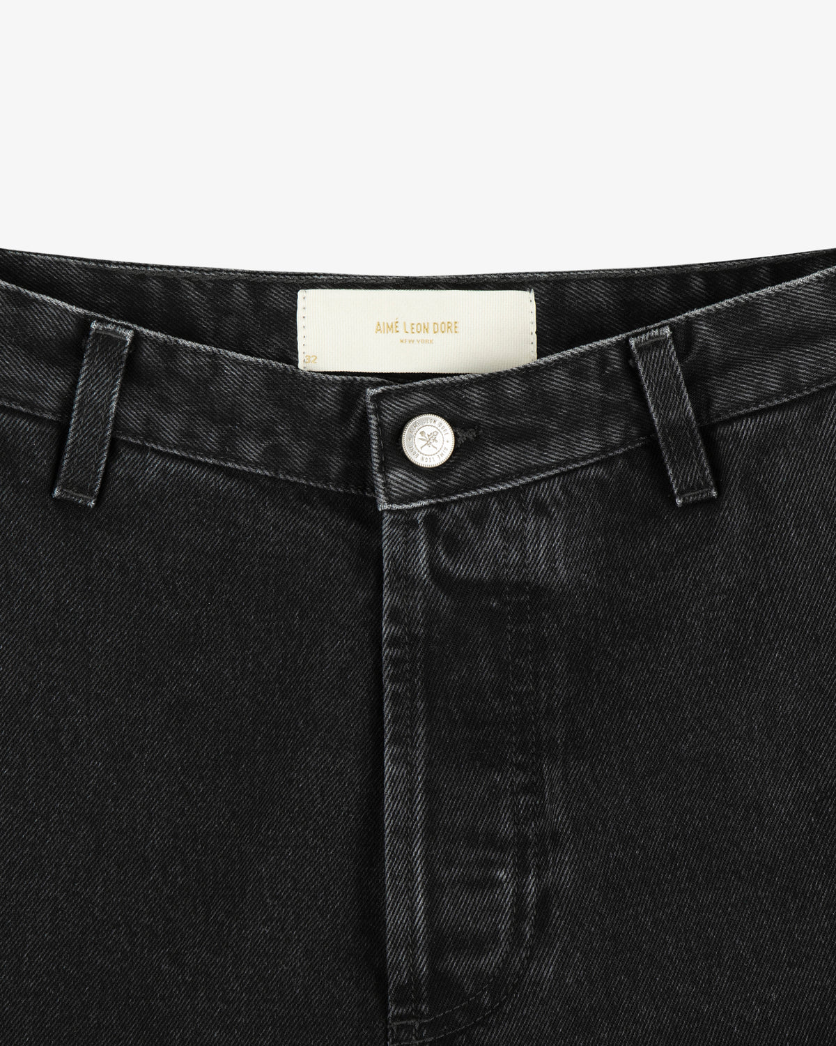 Close-up of the waistband and button of black Denim Carpenter Pant with a visible white Aimé Leon Dore label.
