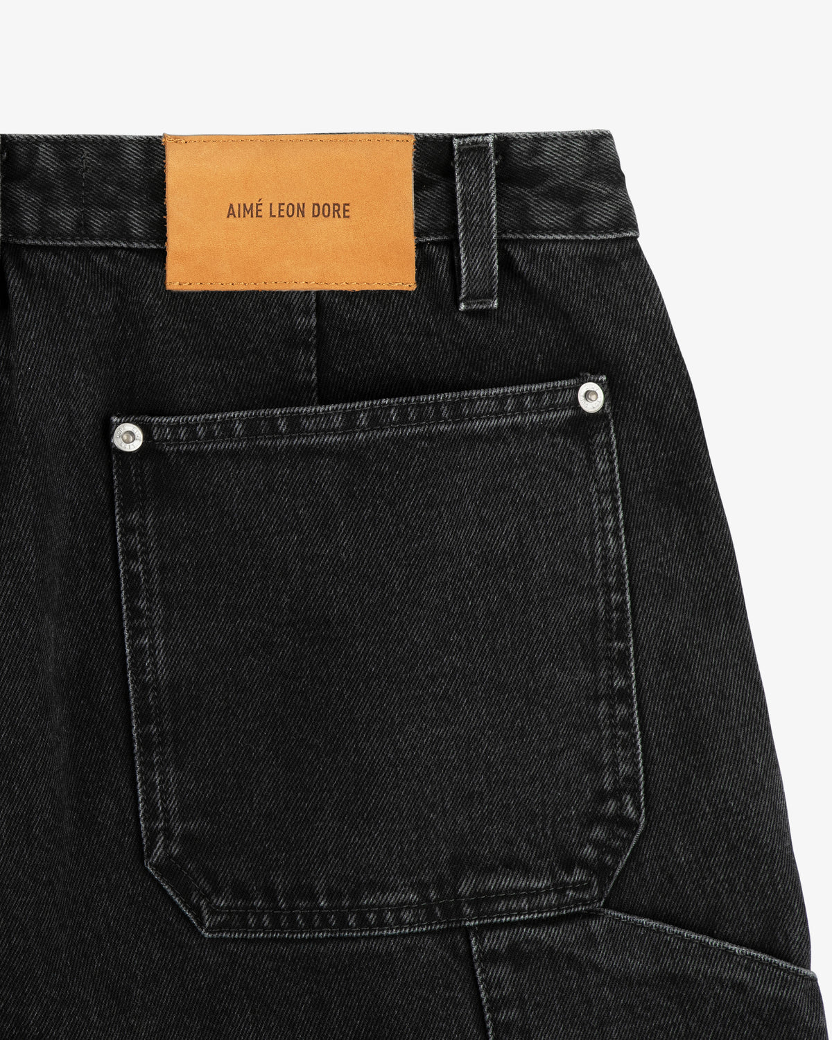 Back pocket of Denim Carpenter Pant with silver rivets and a tan leather AIME LEON DORE patch above the pocket.