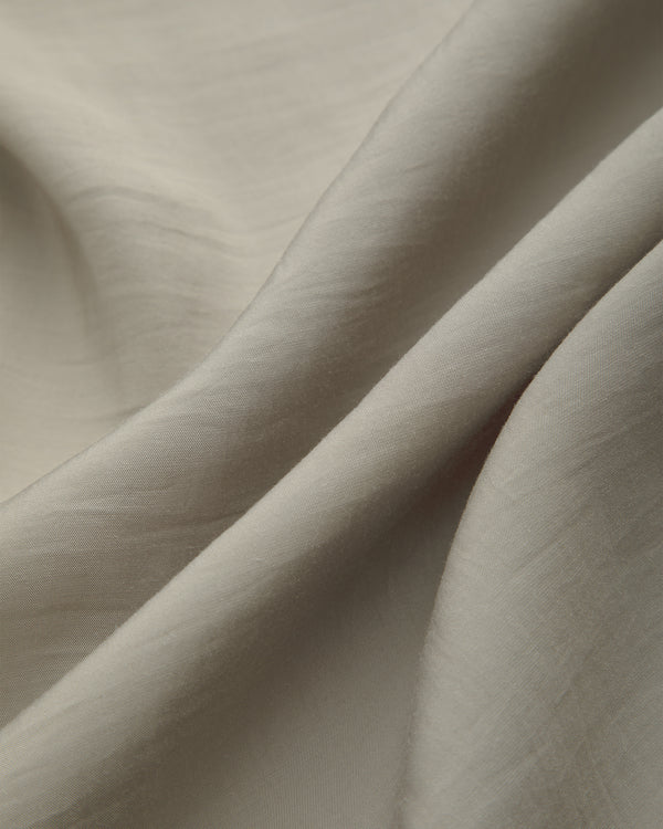 Close-up of Lightweight Leisure Shirt’s beige fabric with soft folds, subtle shadows, and a smooth textured surface.