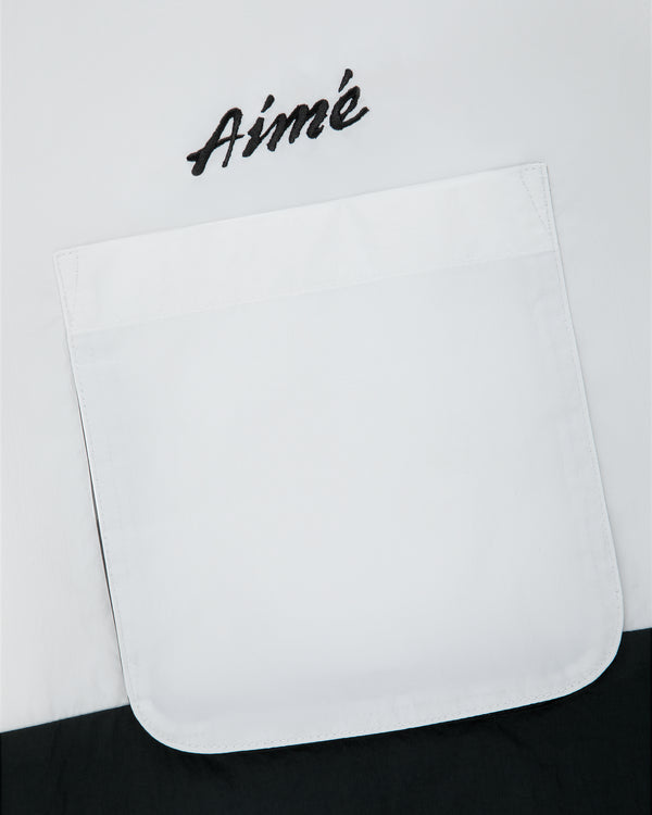 A white pocket on the Colorblock Sport Shirt with “Aimé” embroidered above it in black script.