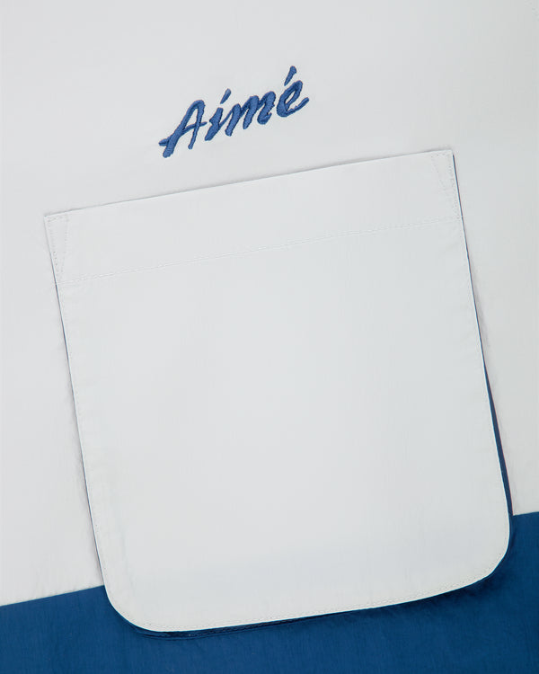Colorblock Sport Shirt with a pocket and Aimé embroidered above it in blue script on white fabric.