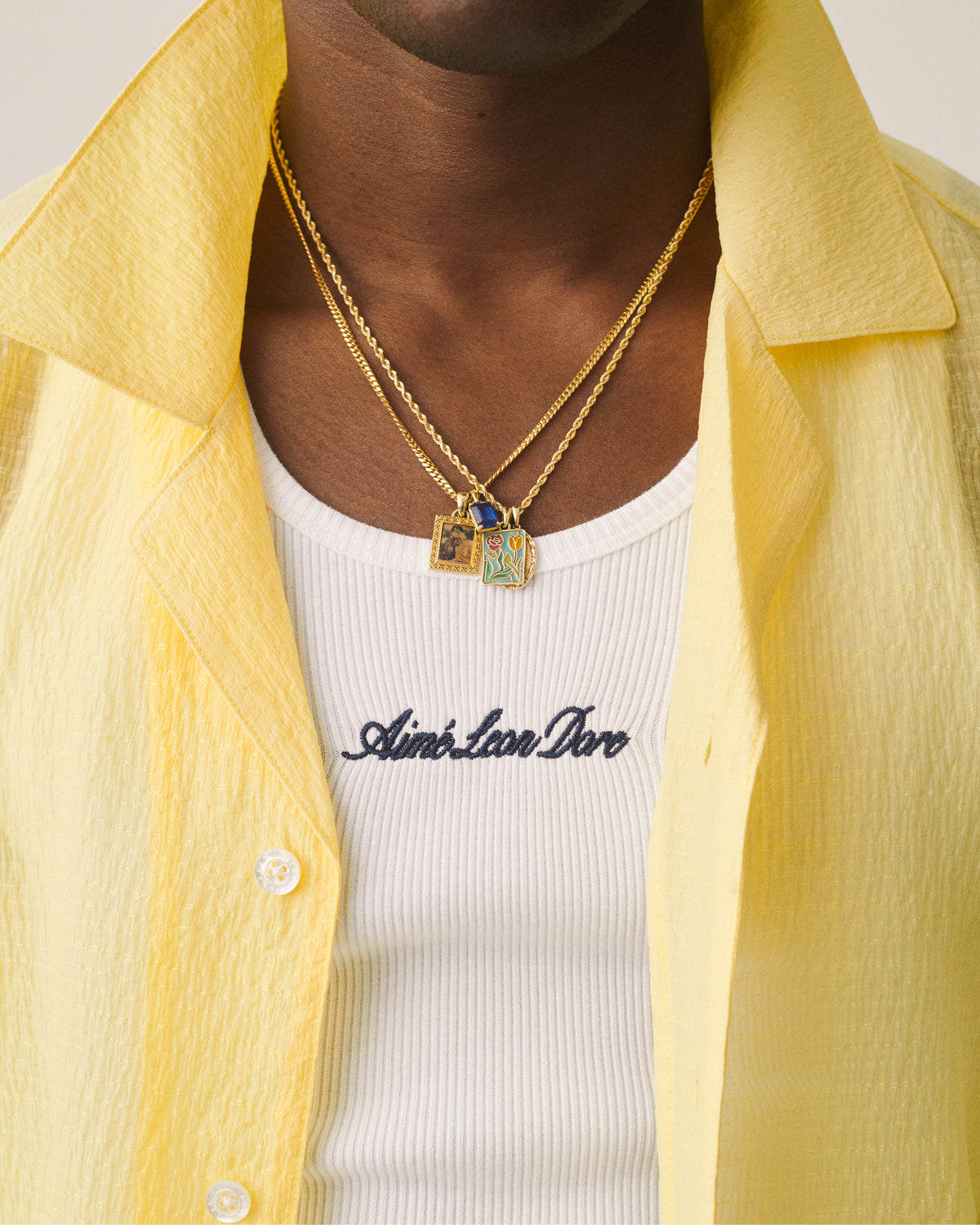 Close-up of a person in a yellow shirt and white tank, layered with gold necklaces featuring the 14Kt Gold Mytilene Pendant.