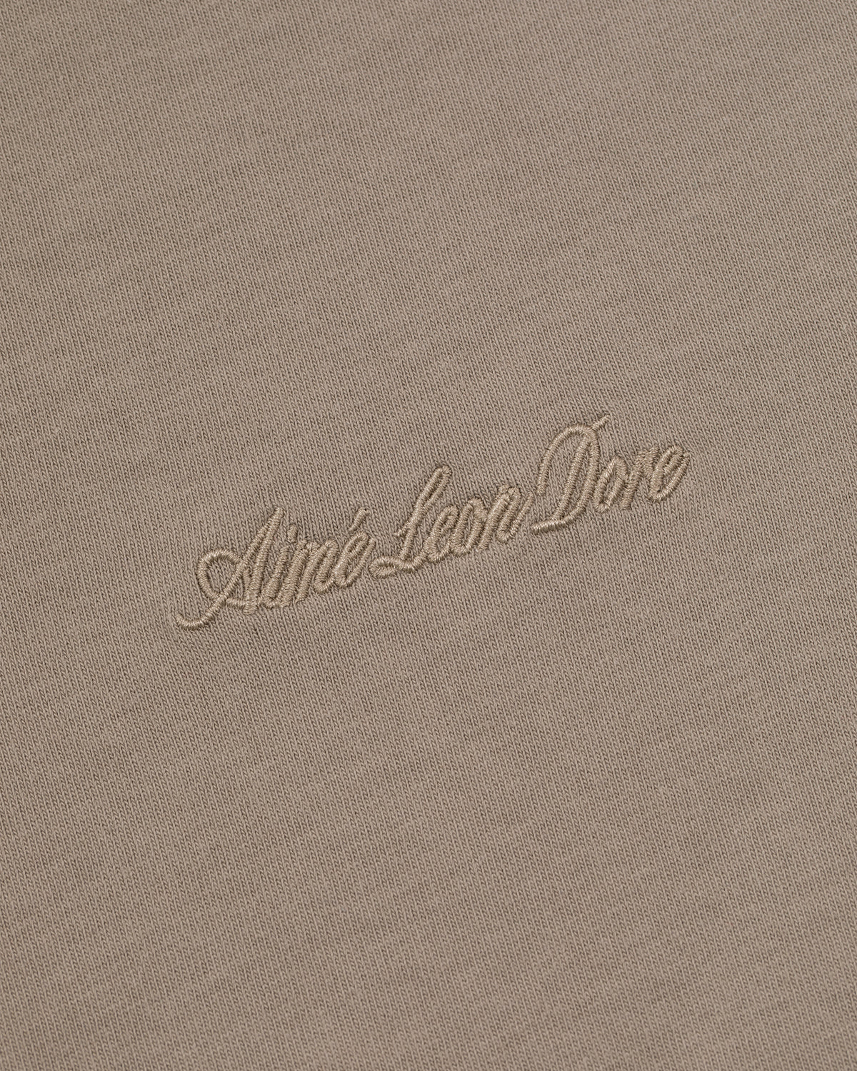 Close-up of beige Embroidered Logo Tee with Aimé Leon Dore stitched in matching cursive thread.