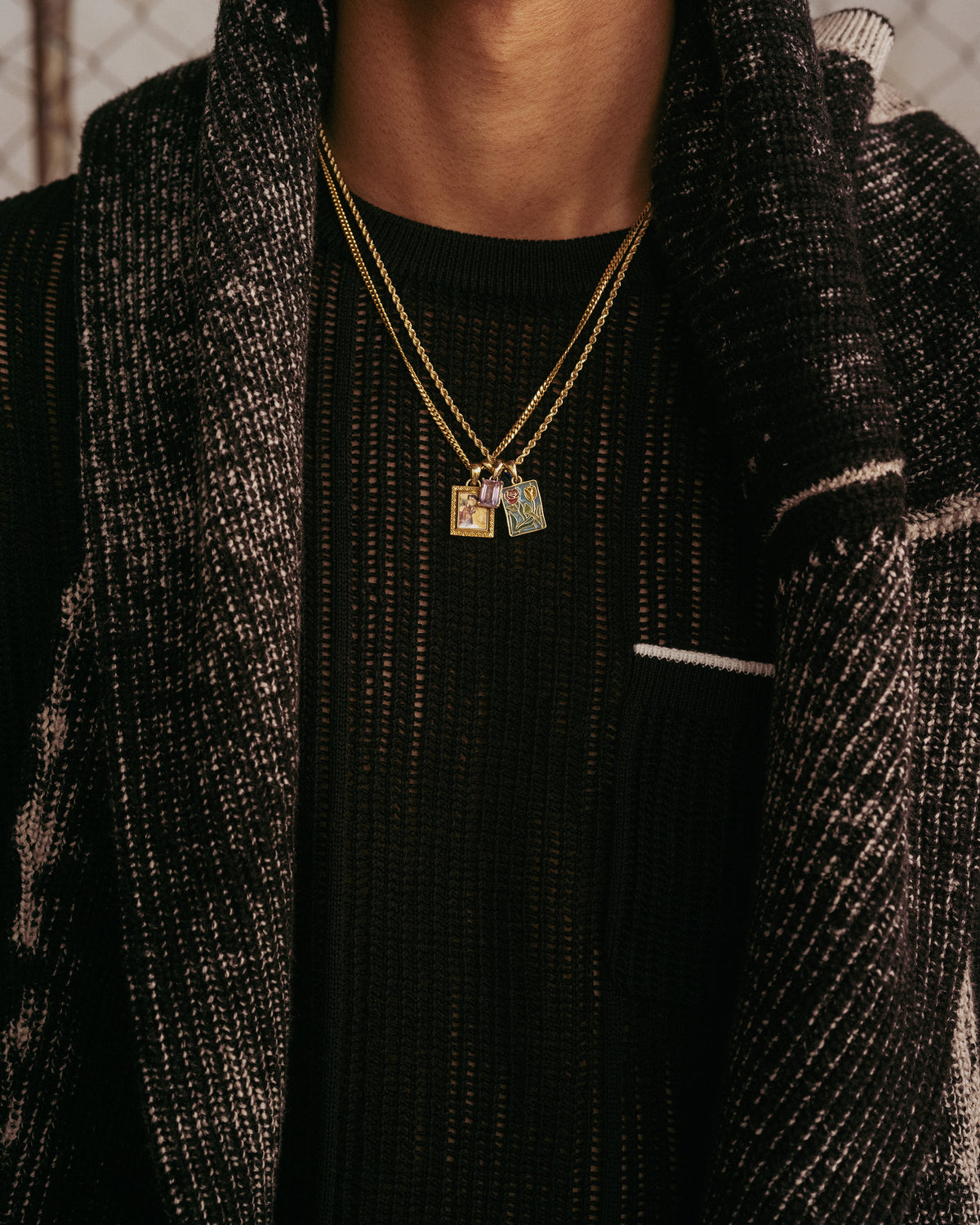 Model wears a 14Kt Gold Stained Glass Crest Pendant, a sheer black shirt, and a textured black and white jacket.