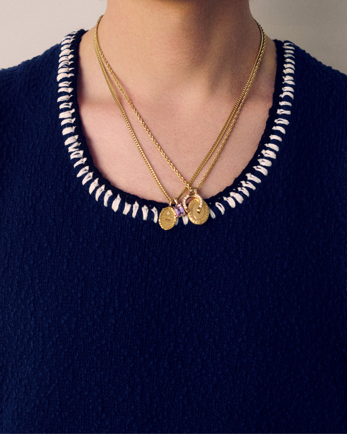 A person wears a navy top with white stitching and two 14Kt Gold Gemstone Pendant necklaces.